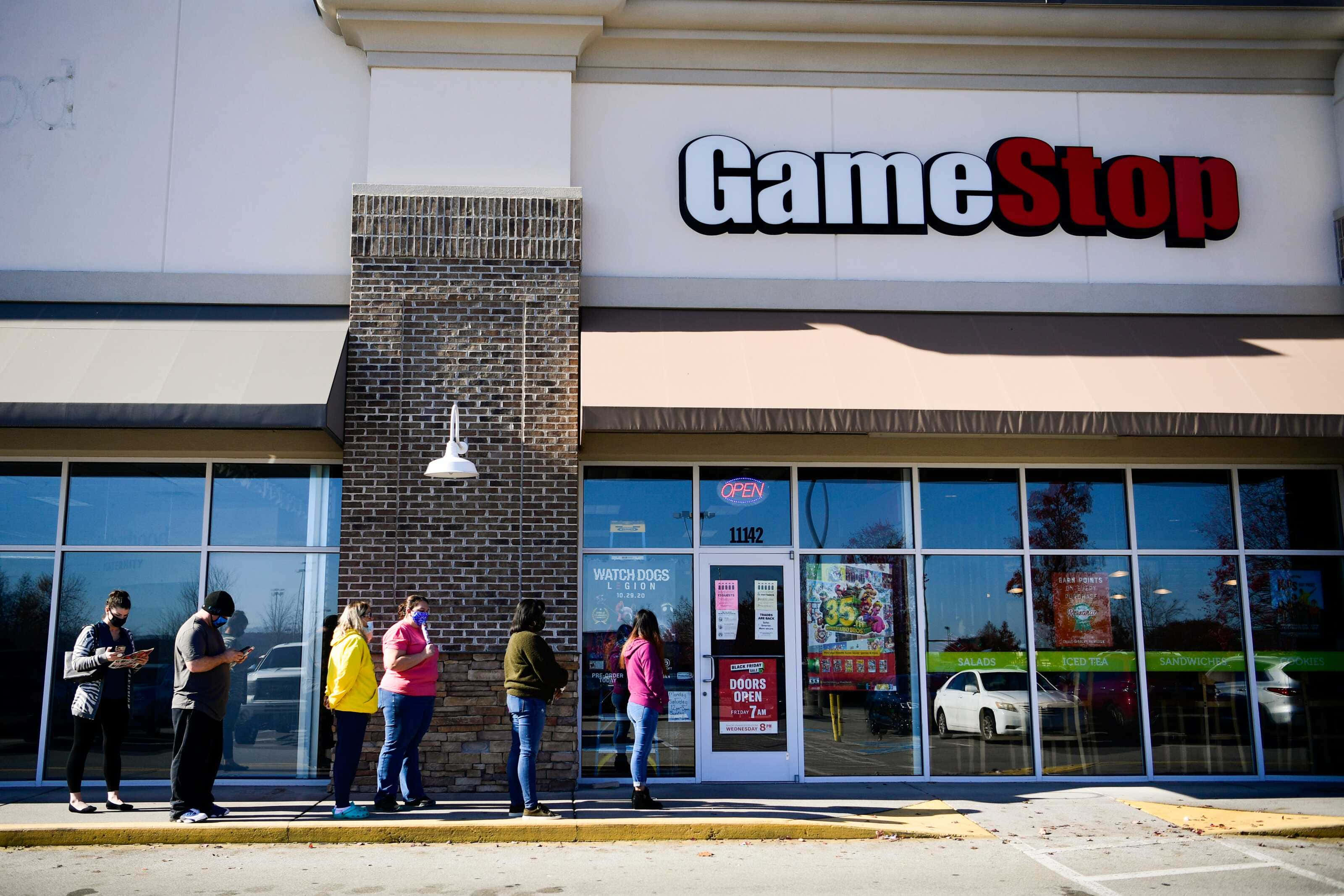 GameStop 桌布 壁紙 — 人們在明亮的日光下於 GameStop 商店外排隊，玻璃窗上有清晰的倒影。