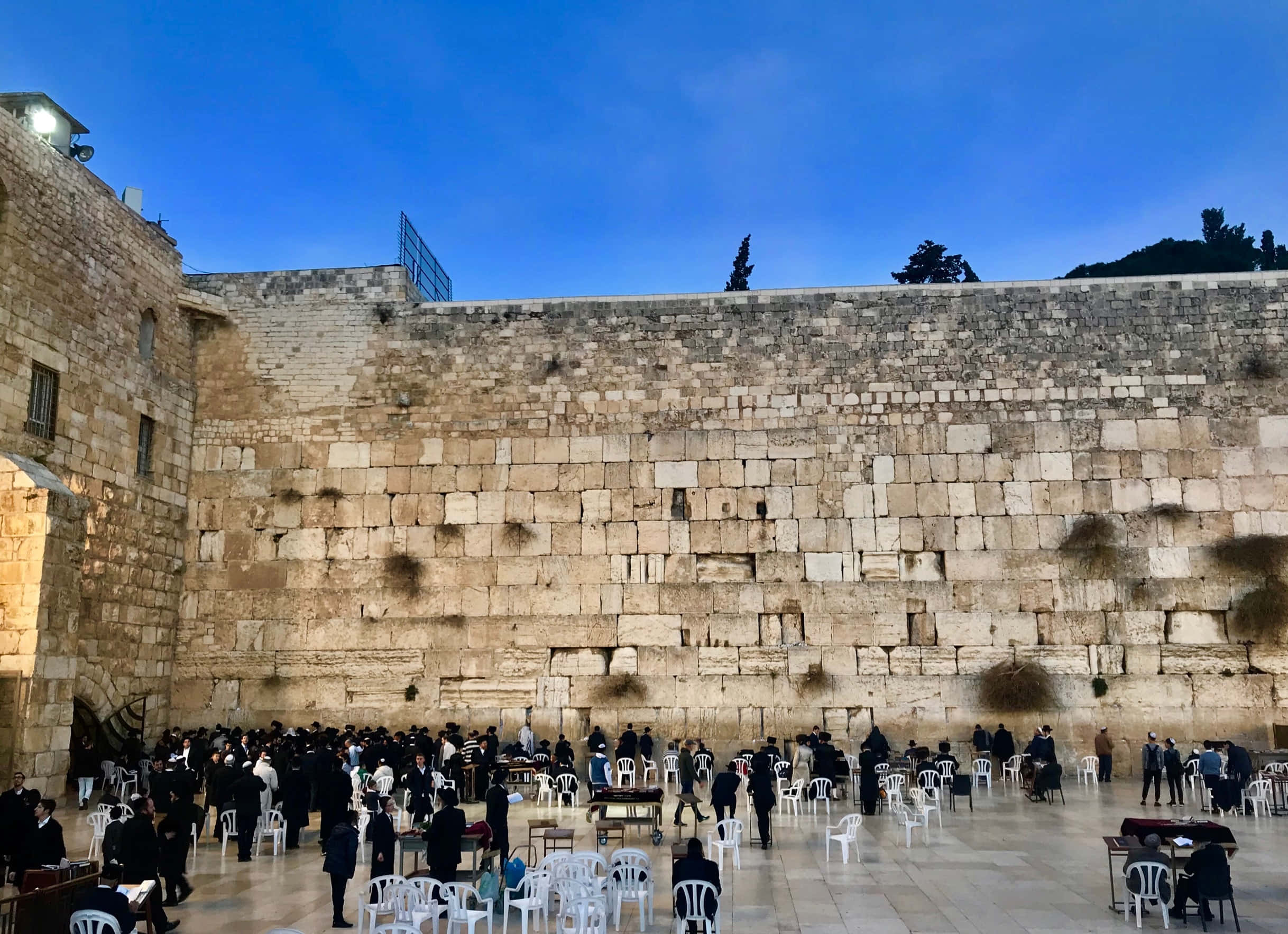 wall 桌布 壁紙 — 人們在晴朗的藍天下聚集在西牆祈禱，古老的石塊高聳在上方。