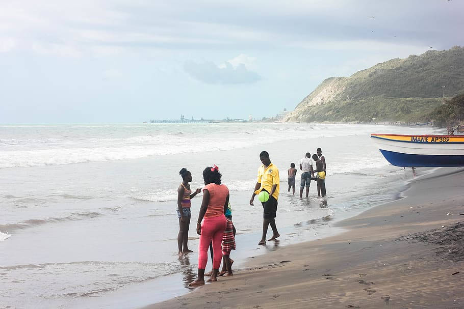 Jamaica 桌布 壁紙 — 人們在沙灘上漫步，溫柔的海浪和色彩繽紛的船隻停泊在附近，天空多雲。