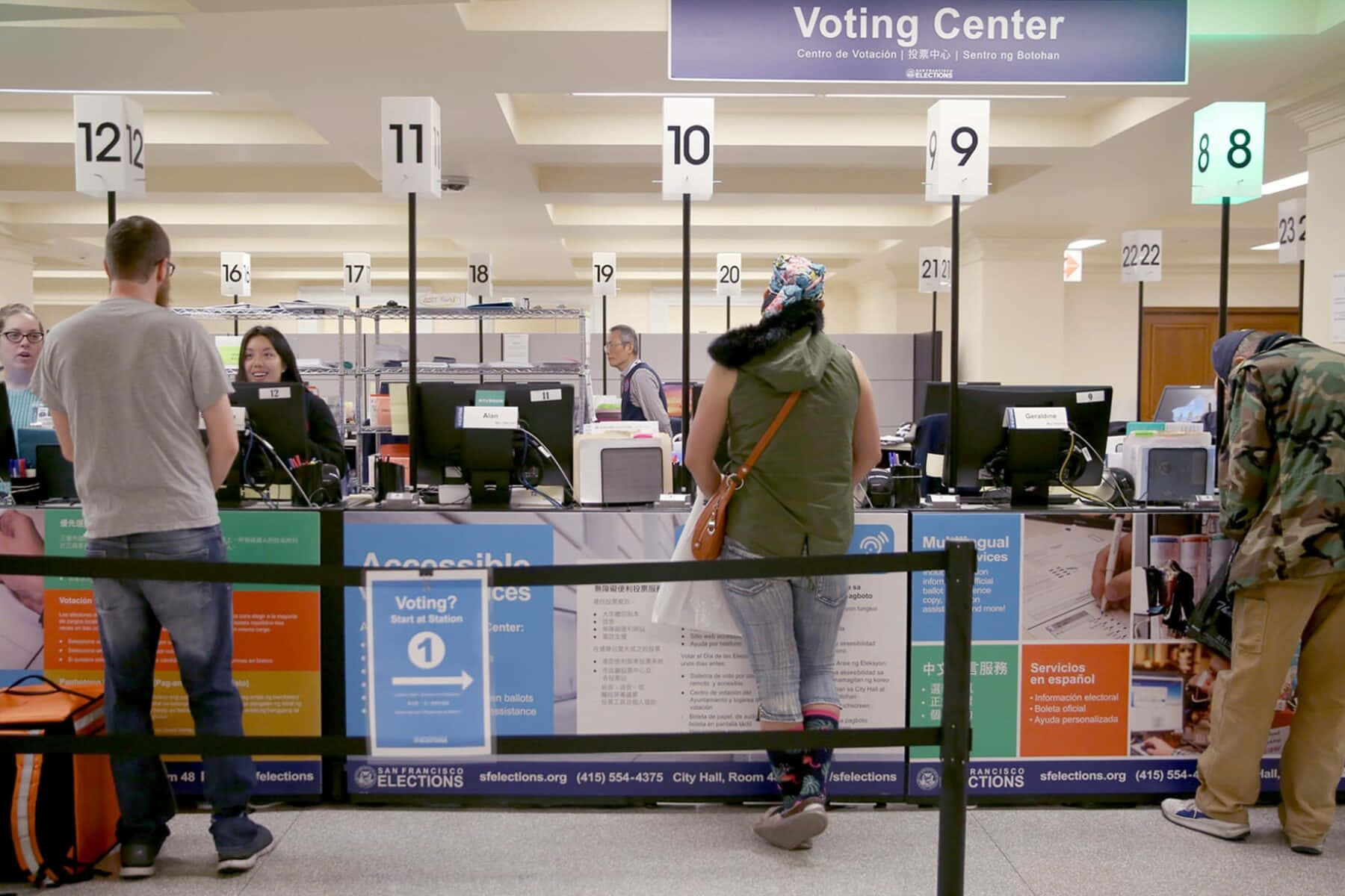 Voting 桌布 壁紙 — 人們在繁忙的舊金山選舉中心內，於有編號的投票間排隊，現場設有多語標示。