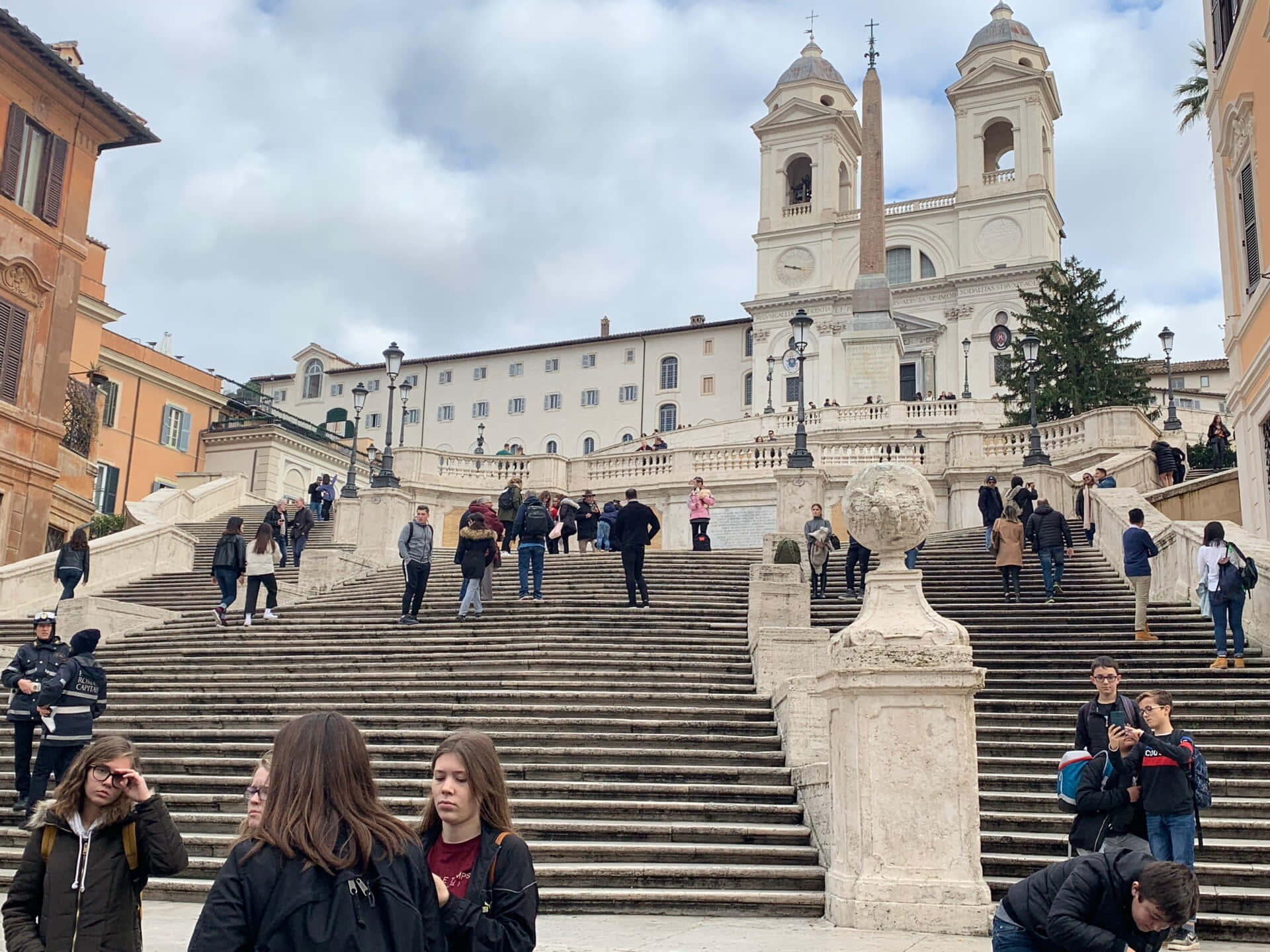 stairs 桌布 壁紙 — 人們在羅馬寬闊的西班牙階梯上上下下，天空多雲，背景有歷史建築和方尖碑。