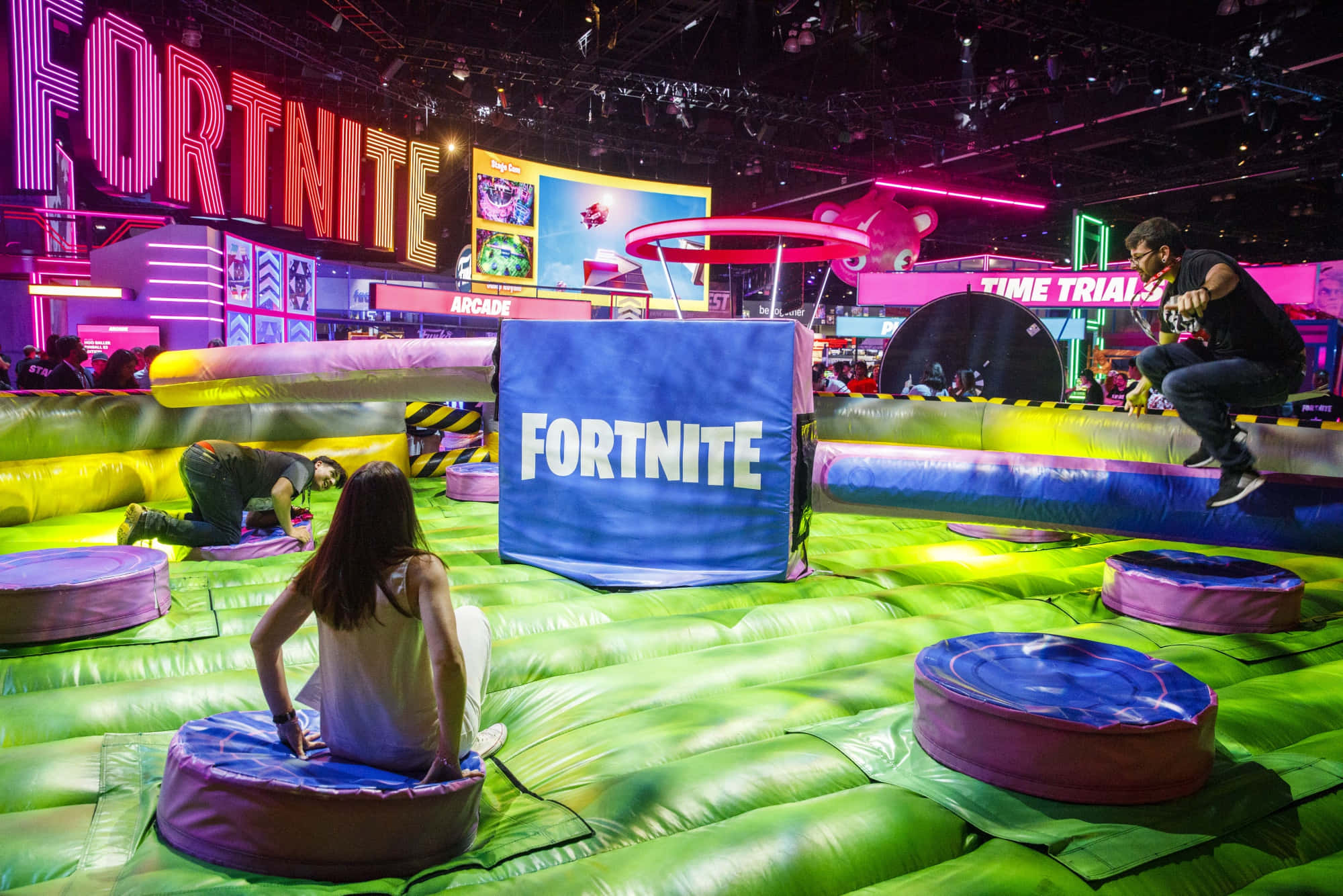 Gaming Conventions 桌布 壁紙 — 人們在遊戲展覽會上，在發光的霓虹燈下，於充滿活力的Fortnite充氣障礙賽道上玩耍。