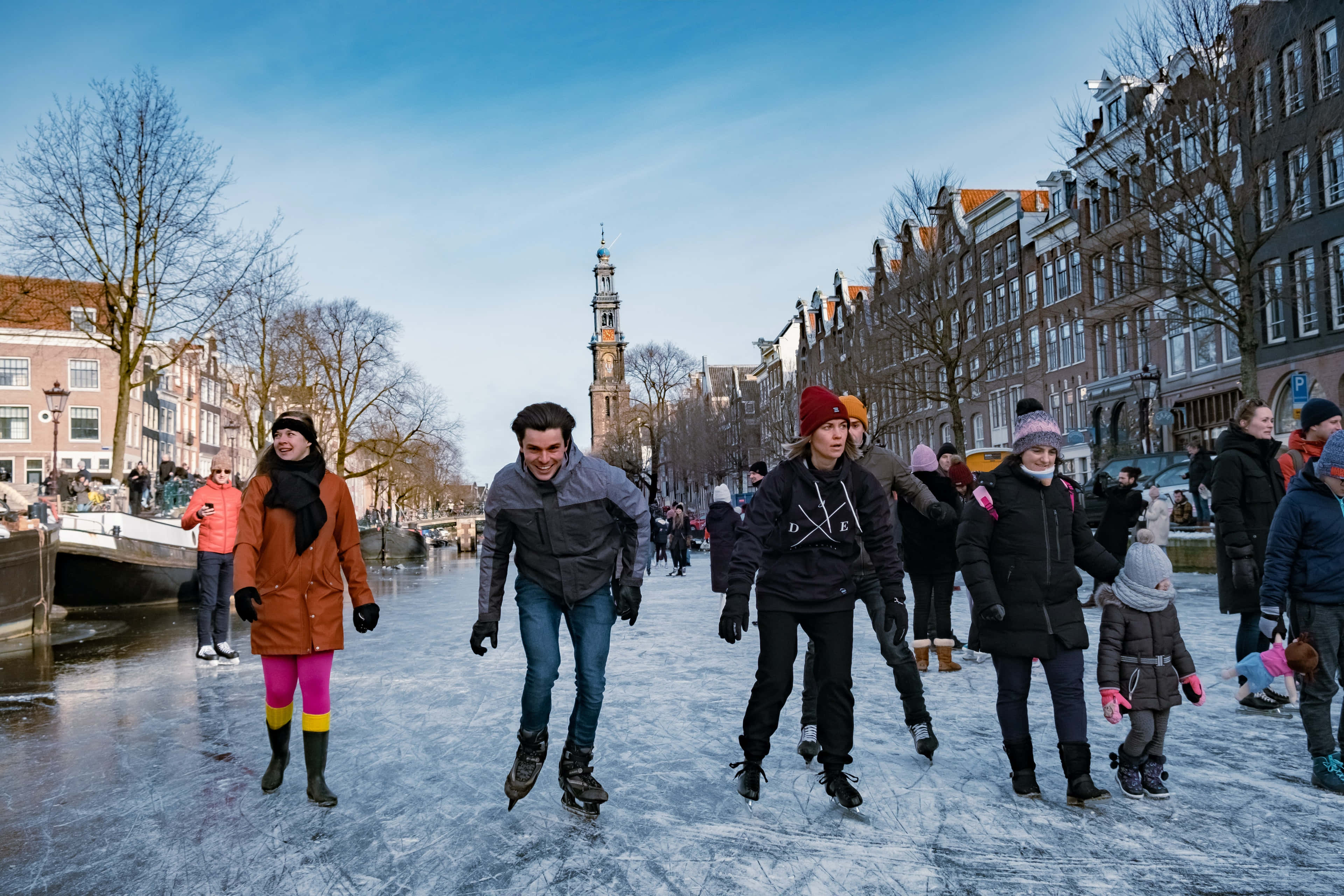 Winter 桌布 壁紙 — 人們在阿姆斯特丹結冰的運河上，在晴朗的藍天下愉快地溜冰。
