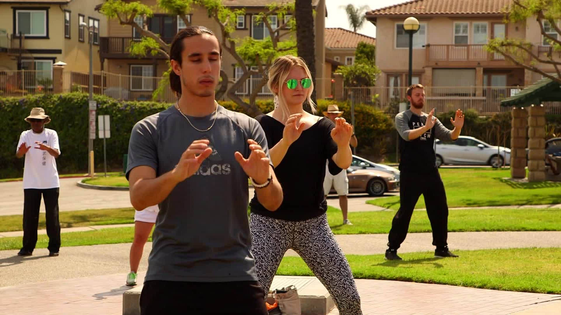 martial arts 桌布 壁紙 — 人們在陽光明媚的住宅公園裡練習戶外瑜伽，背景有棕櫚樹和公寓大樓。