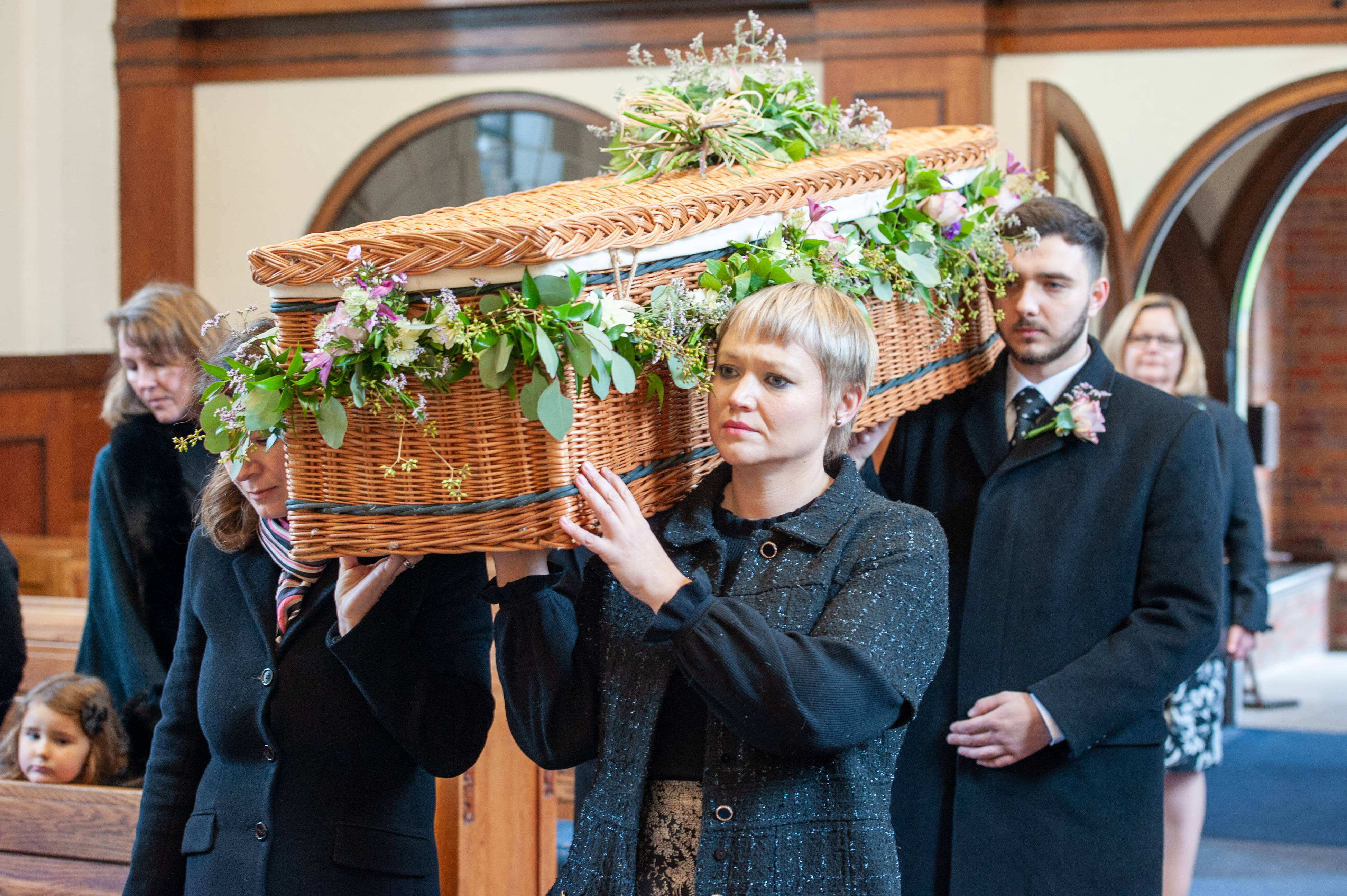 Funeral 桌布 壁紙 — 人們莊嚴地抬著一個飾有鮮花的柳條棺材穿過木製教堂內部。