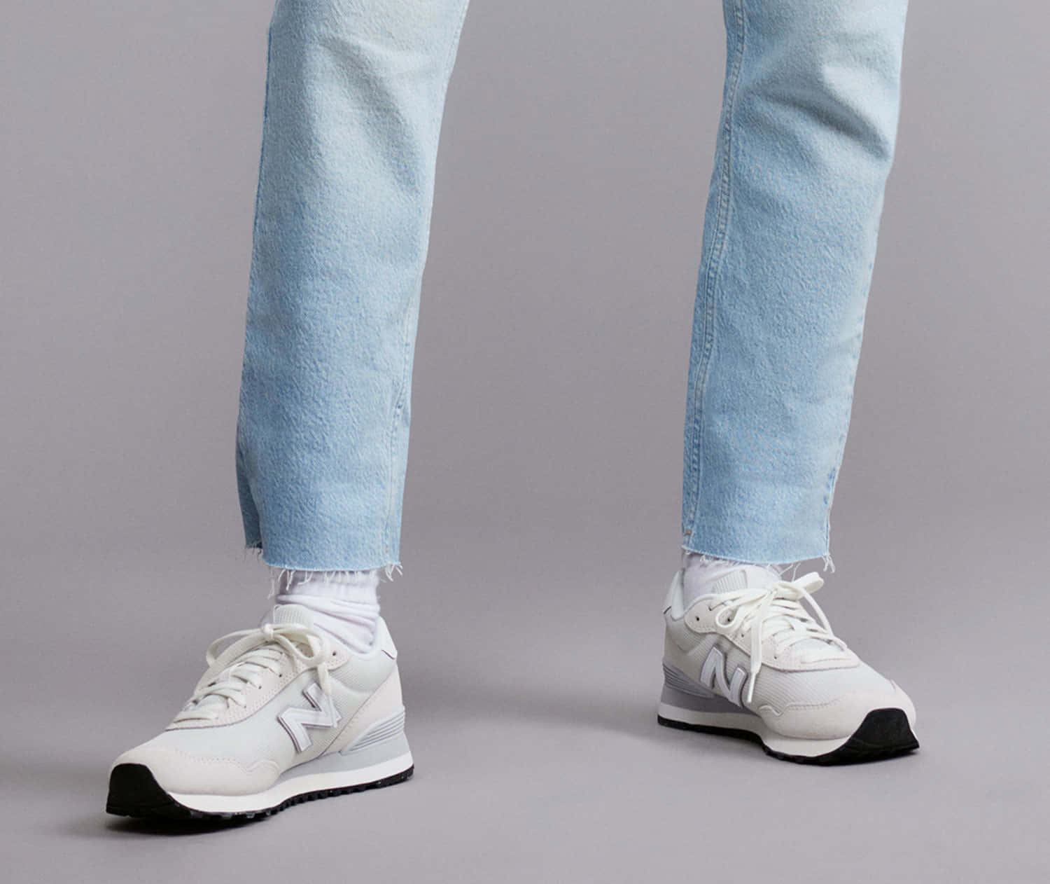 New Balance 桌布 壁紙 — 人物穿著淺藍色牛仔褲和白色New Balance運動鞋的特寫，背景為中性灰色。
