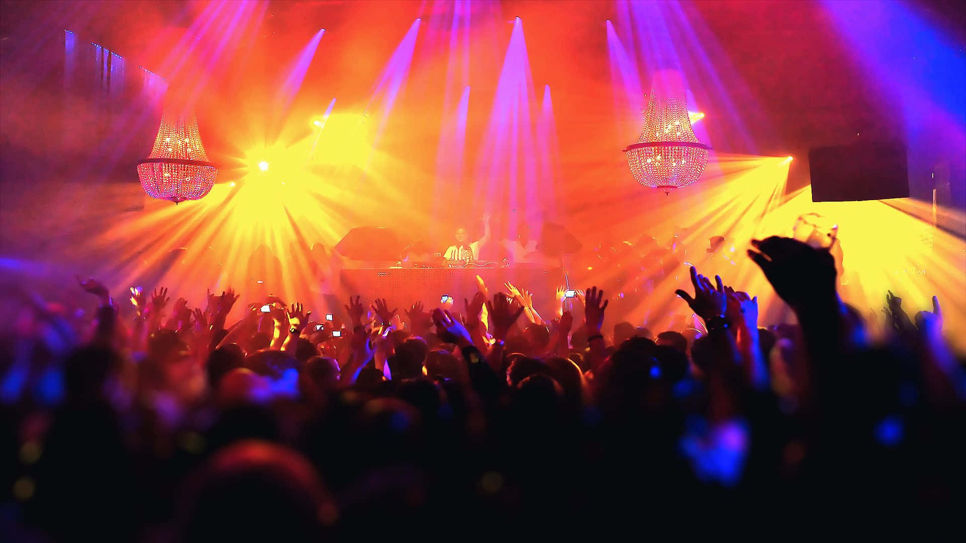 Club Party 桌布 壁紙 — 人群剪影在音樂會上，在充滿活力的橙色紫色舞台燈光和吊燈下舉起雙手。