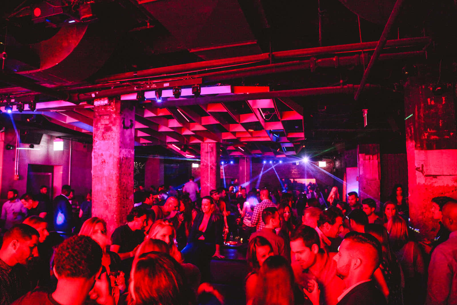 club 桌布 壁紙 — 人群在充滿工業風、帶有裸露橫樑和混凝土柱的粗獷夜店中，隨著脈動的紅光起舞。