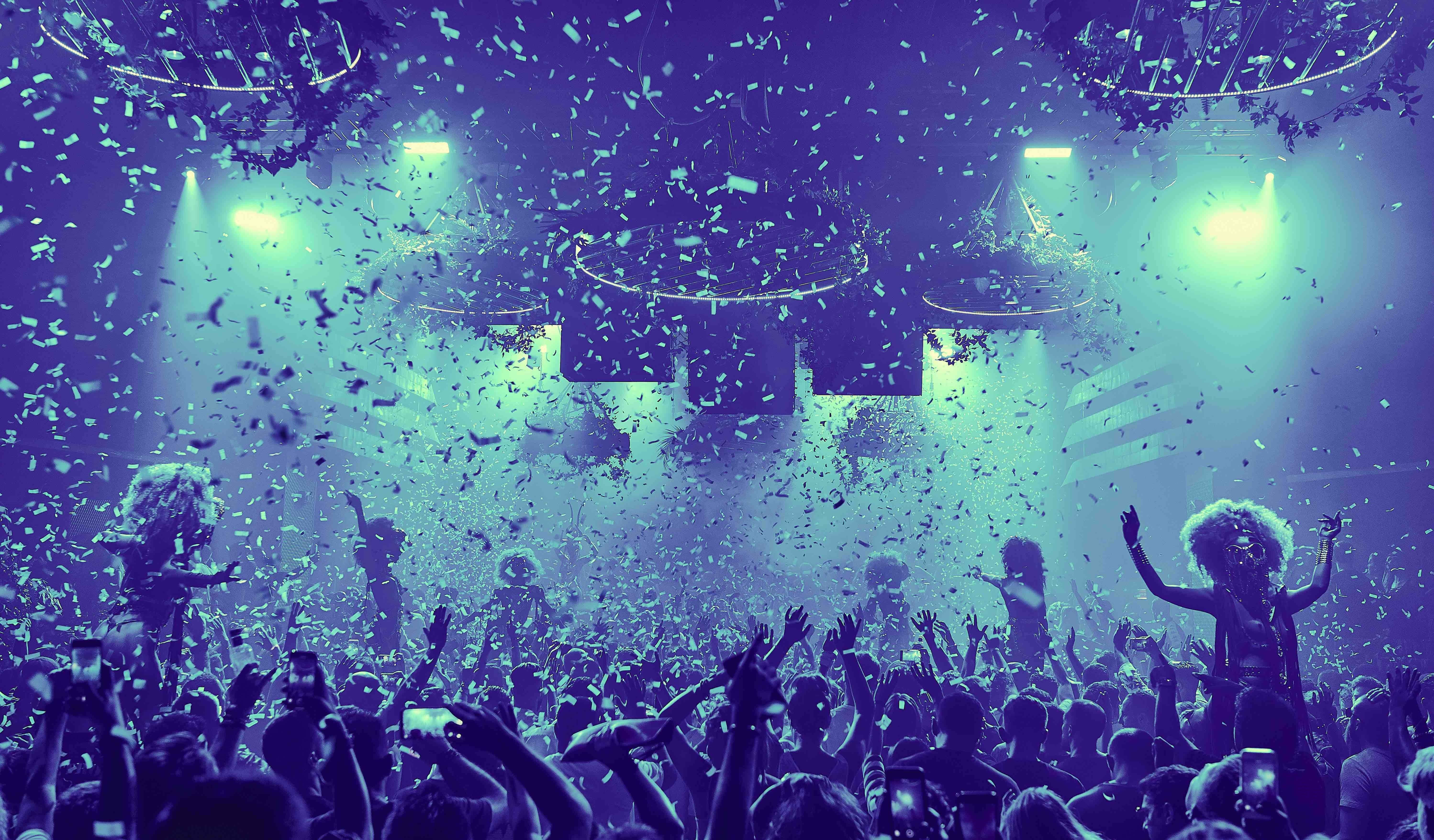 Confetti 桌布 壁紙 — 人群在充滿活力的夜總會中，在發光的綠色燈光下跳舞，五彩紙屑如雨般落下，形成一場電光火石的慶祝。