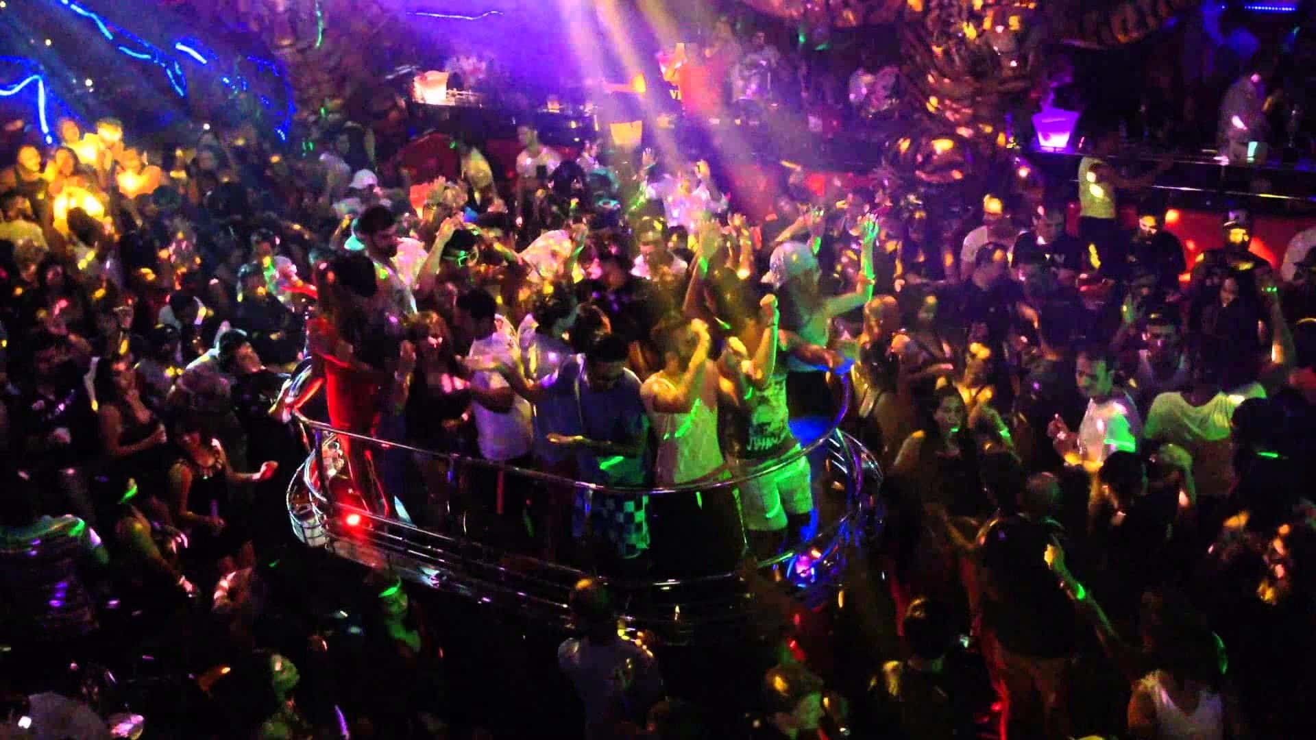 Club Party 桌布 壁紙 — 人群在充滿活力的霓虹燈下，在擠滿人的夜總會中跳舞，帶有發光效果。