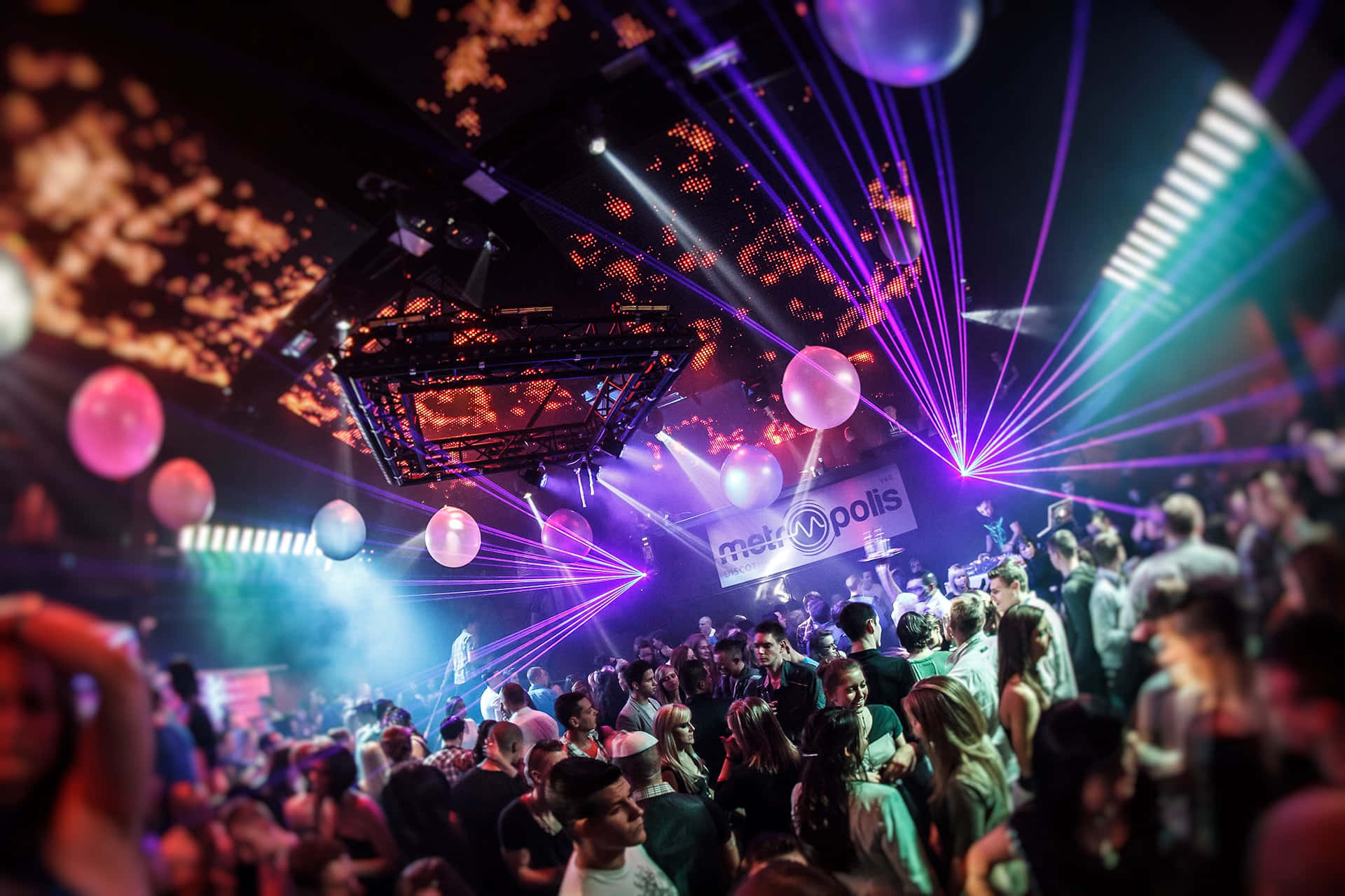 club 桌布 壁紙 — 人群在擠滿人的夜總會中，在充滿活力的紫色雷射燈光和漂浮的氣球下跳舞。