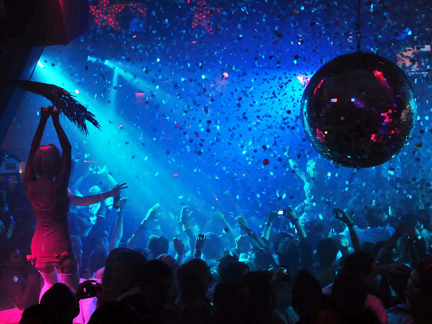Nightclub 桌布 壁紙 — 人群在旋轉的迪斯可球下跳舞，五彩紙屑在藍色和粉紅色燈光籠罩的充滿活力的夜總會中飄落。
