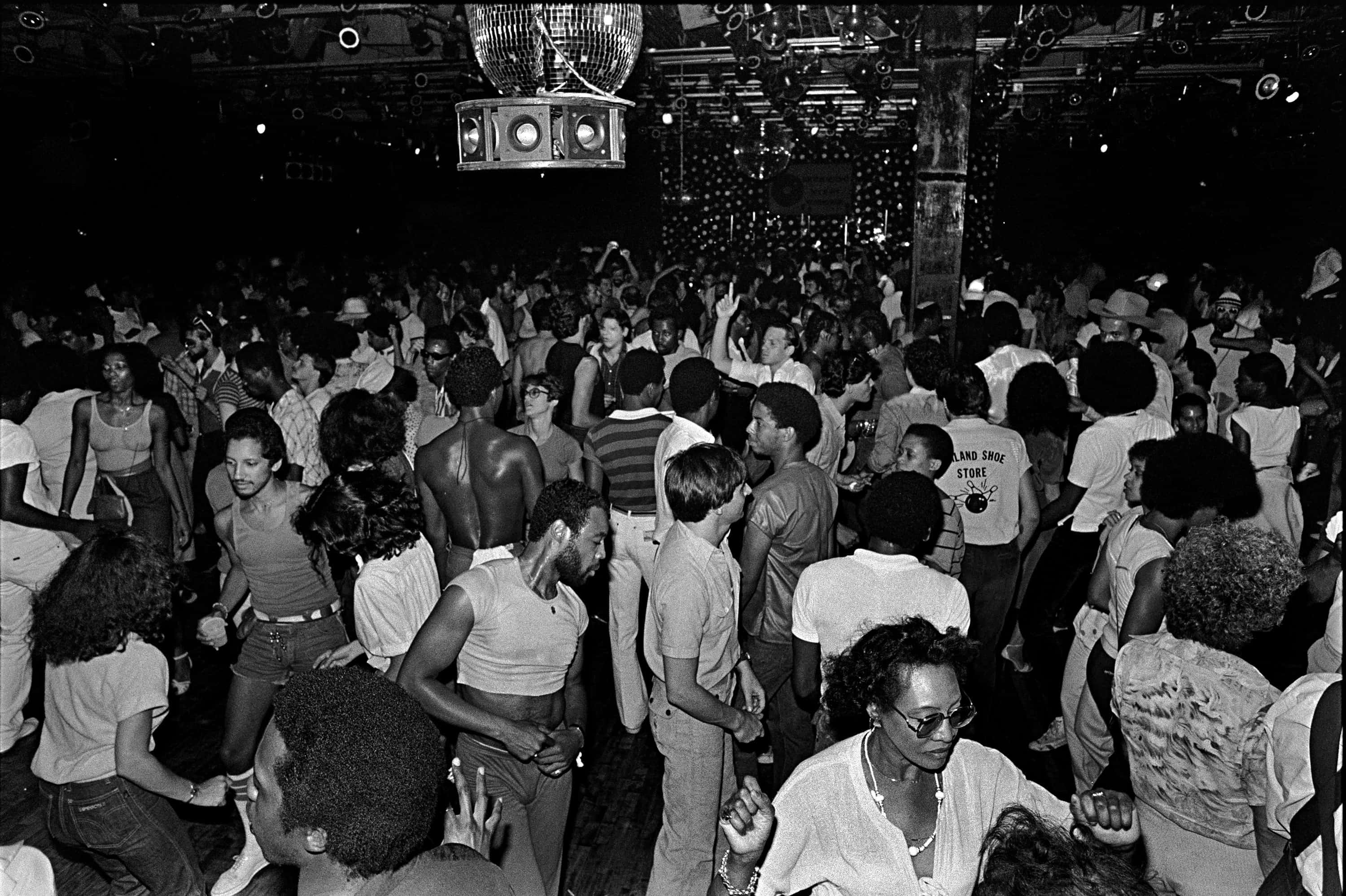 1980s 桌布 壁紙 — 人群在昏暗的1970年代夜總會中，在迪斯科球下舉手跳舞，充滿活力。