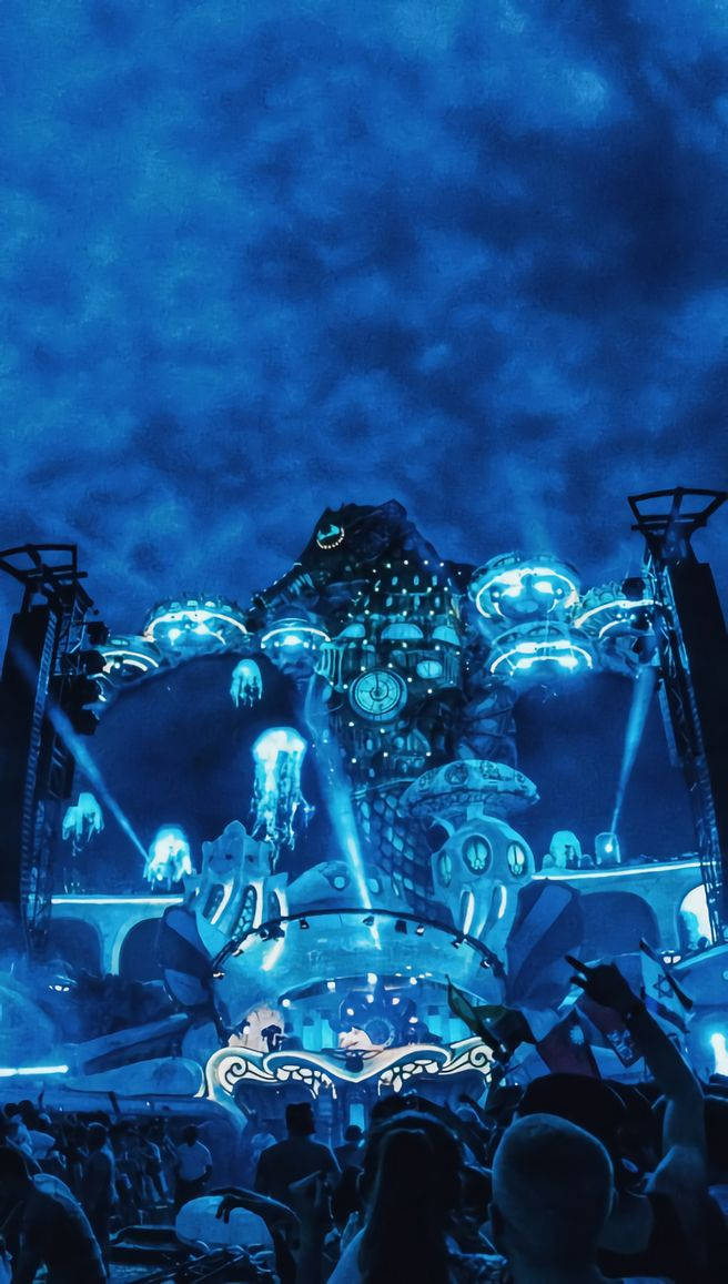 Tomorrowland 桌布 壁紙 — 人群在暴風雨夜空下，湧向一座高聳、發光的藍色舞台結構，該結構形狀像一個奇幻的機械生物。