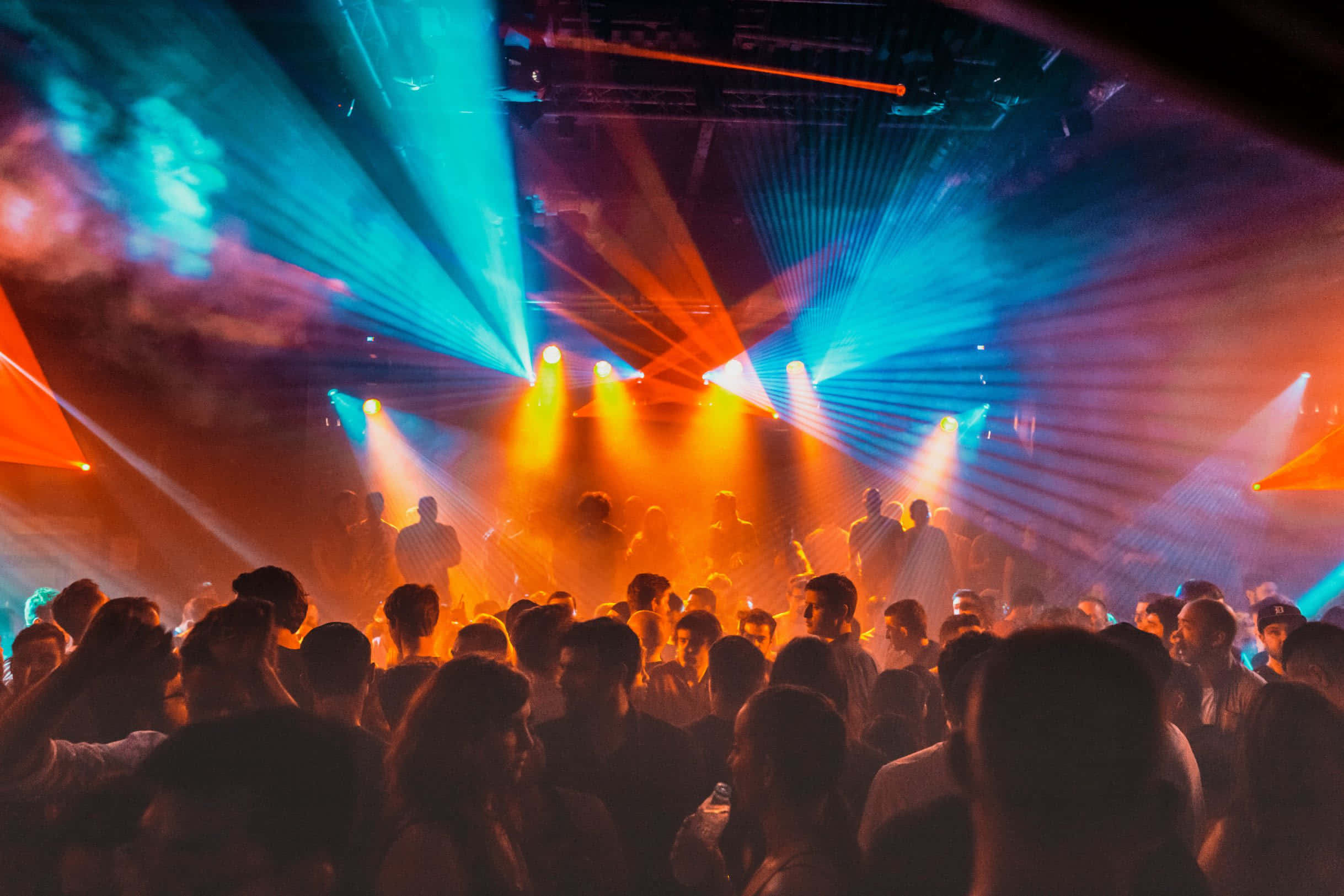 Nightclub 桌布 壁紙 — 人群在煙霧瀰漫的夜總會中，在充滿活力的藍色和橙色雷射燈光下跳舞。