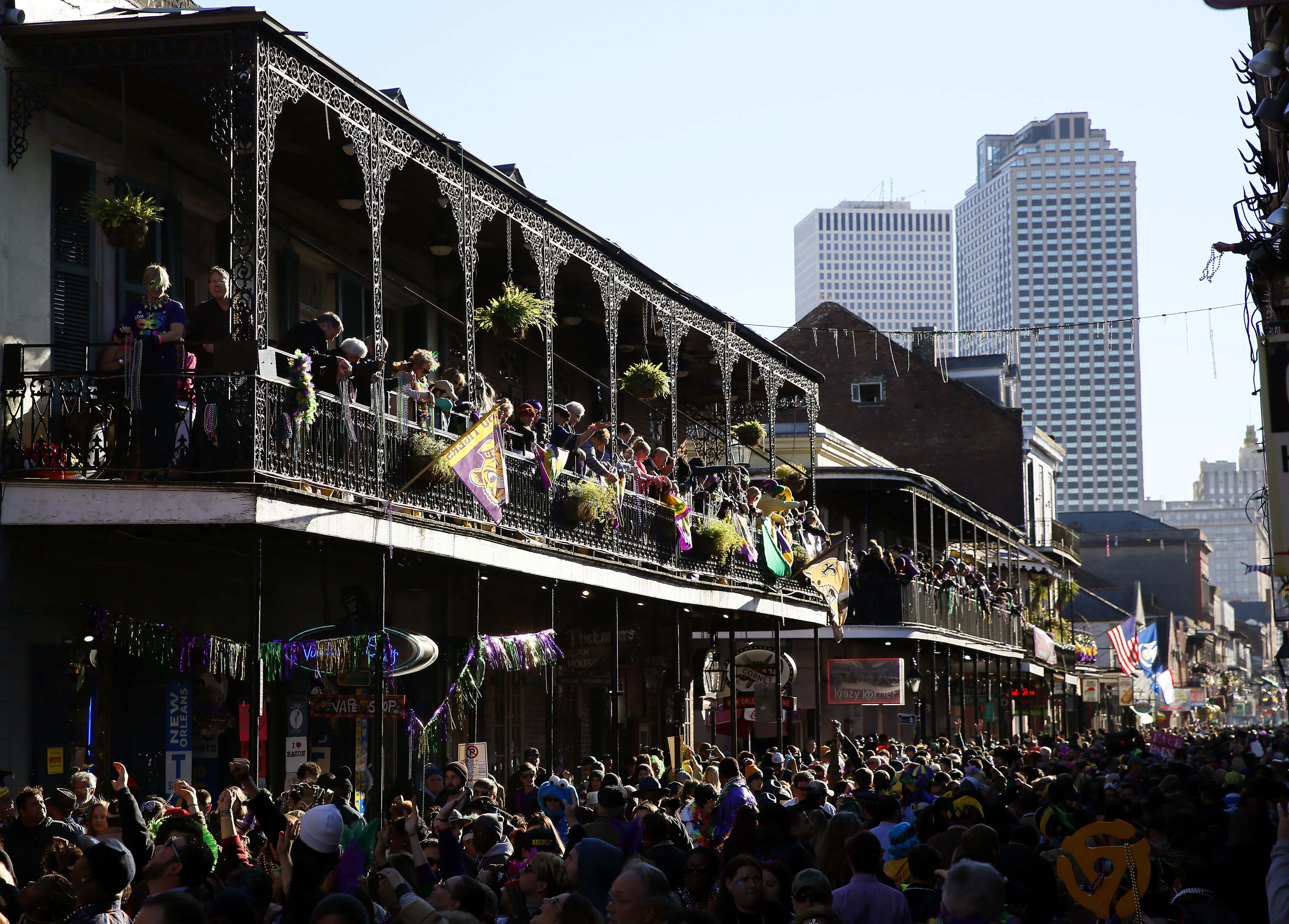 Mardi Gras 桌布 壁紙 — 人群在燦爛陽光下慶祝熱鬧的街頭遊行，華麗的陽台俯瞰著節日場景。