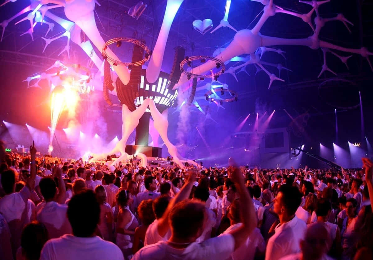Nightclub 桌布 壁紙 — 人群在發光的紫色和橙色舞台燈光下湧動，下方是巨大的骷髏雕塑，在銳舞派對中。