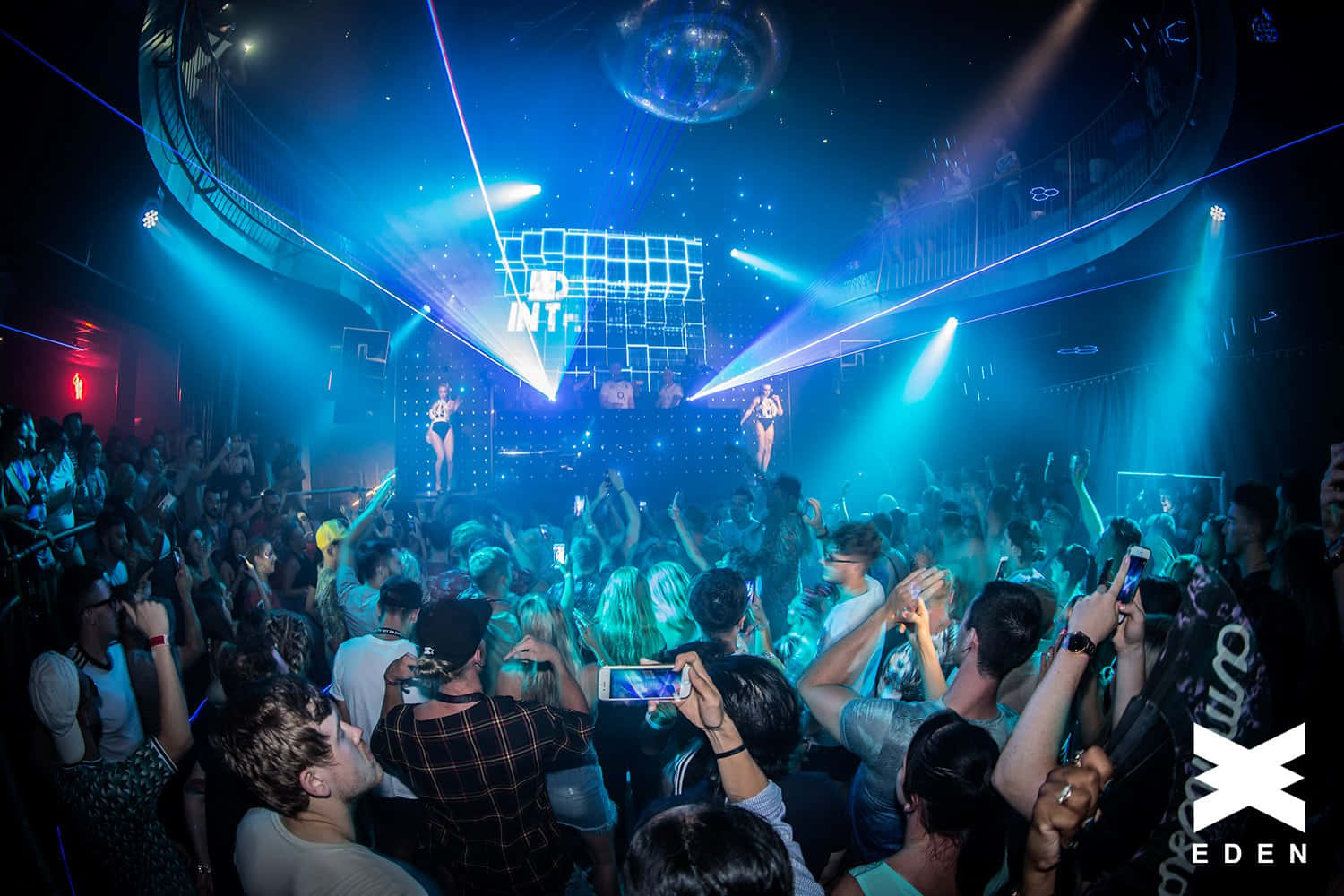 Nightclub 桌布 壁紙 — 人群在藍色雷射燈光和迪斯可球下跳舞，夜店擠滿了人，舞台上有表演者。