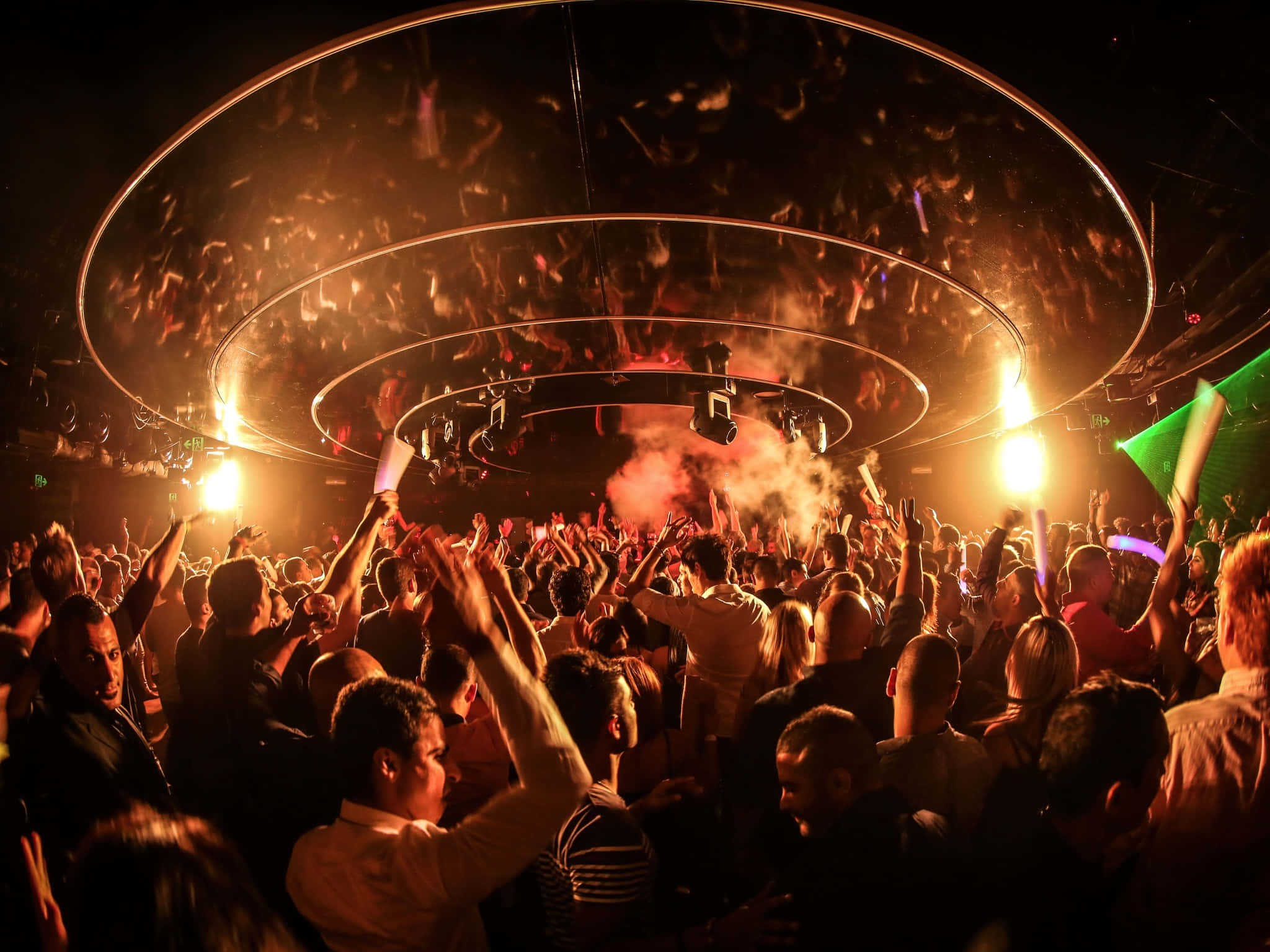 Nightclub 桌布 壁紙 — 人群在黑暗的夜總會中，在發光的圓形燈光下跳舞，伴隨著煙霧和高舉的雙手。