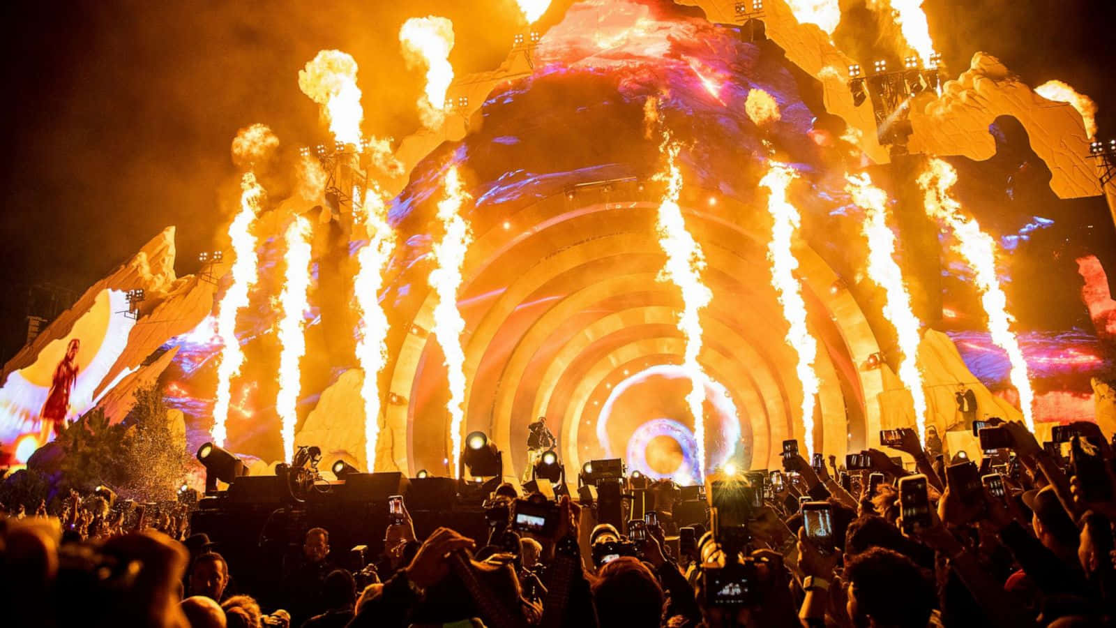 Astroworld 桌布 壁紙 — 人群捕捉到夜間大型演唱會舞台，帶有熾熱的煙火和發光的圓形燈光。