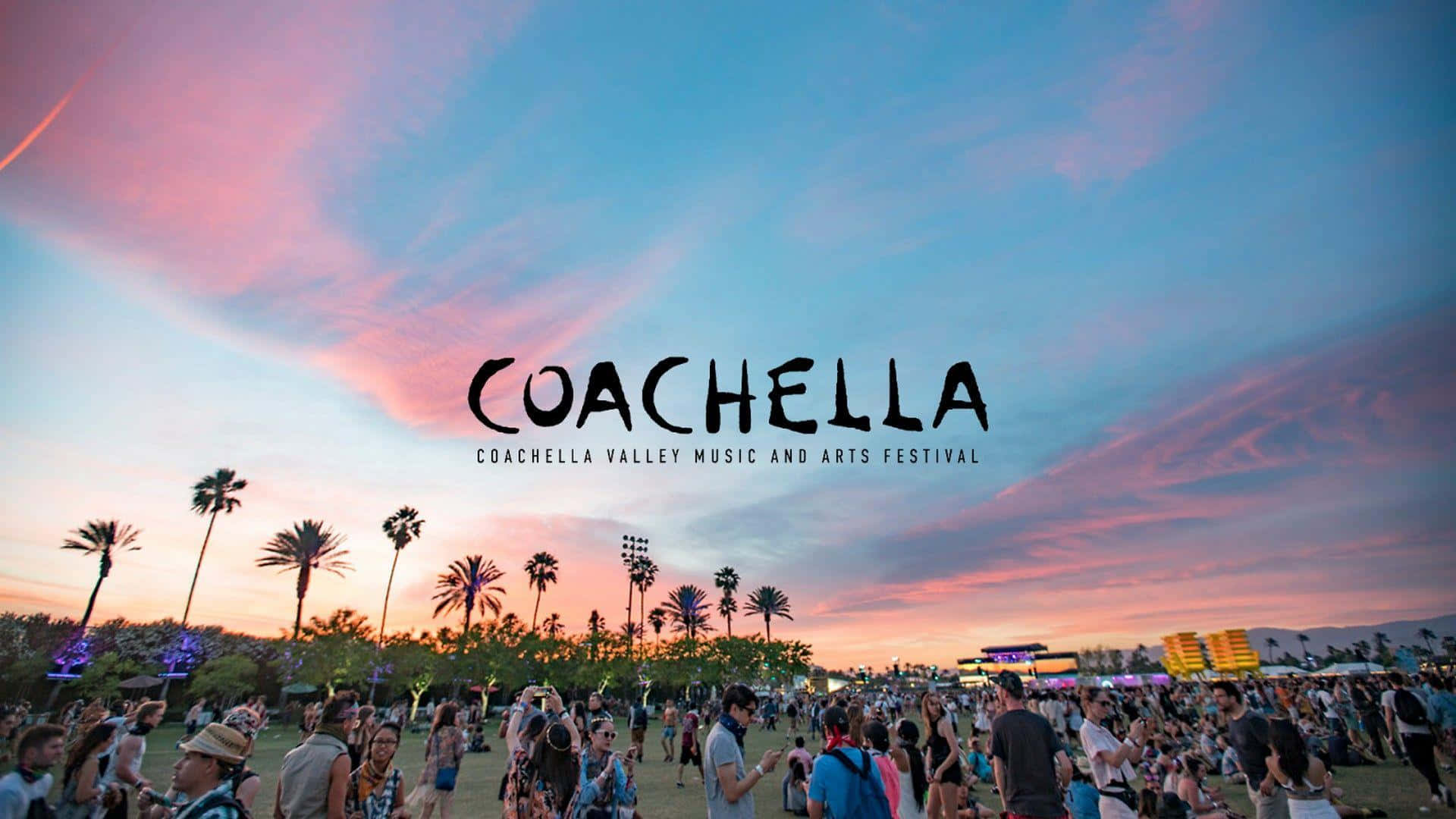 Coachella 桌布 壁紙 — 人群聚集在充滿活力的粉紅色和藍色日落天空下，棕櫚樹在科切拉音樂節上形成剪影。