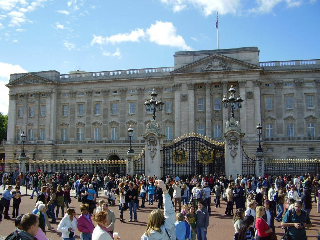 England 桌布 壁紙 — 人群聚集在白金漢宮宏偉的石砌外牆前，天空湛藍，白雲點點。