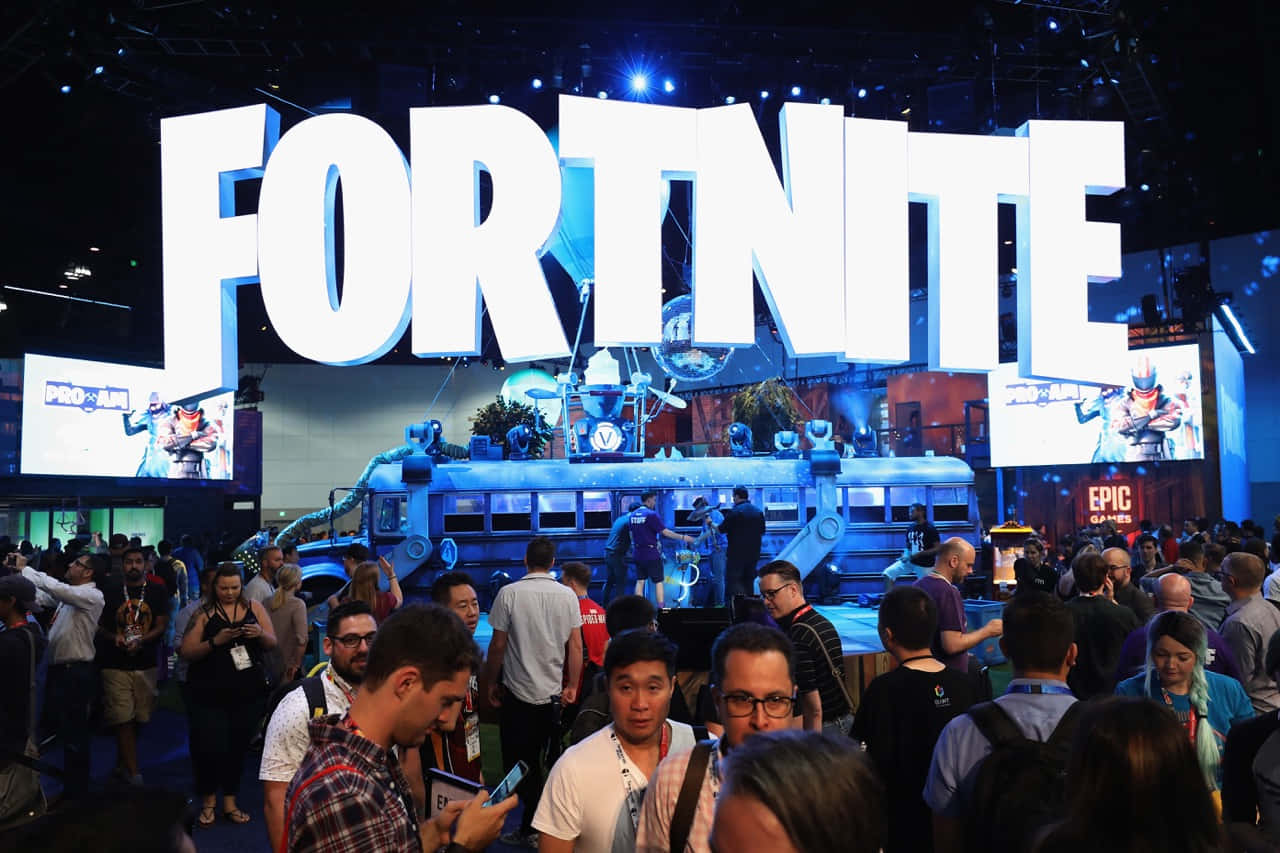 Gaming Conventions 桌布 壁紙 — 人群聚集在繁忙的遊戲展會中，藍色舞台燈光下巨大的白色「FORTNITE」字母下方。