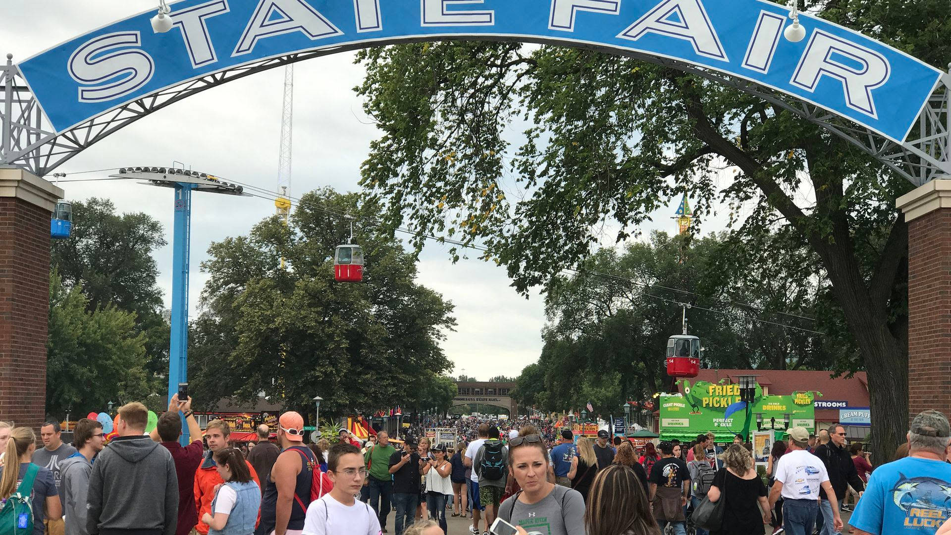 Minnesota 桌布 壁紙 — 人群聚集在藍色的State Fair拱門下，纜車在多雲的天空下滑過頭頂。