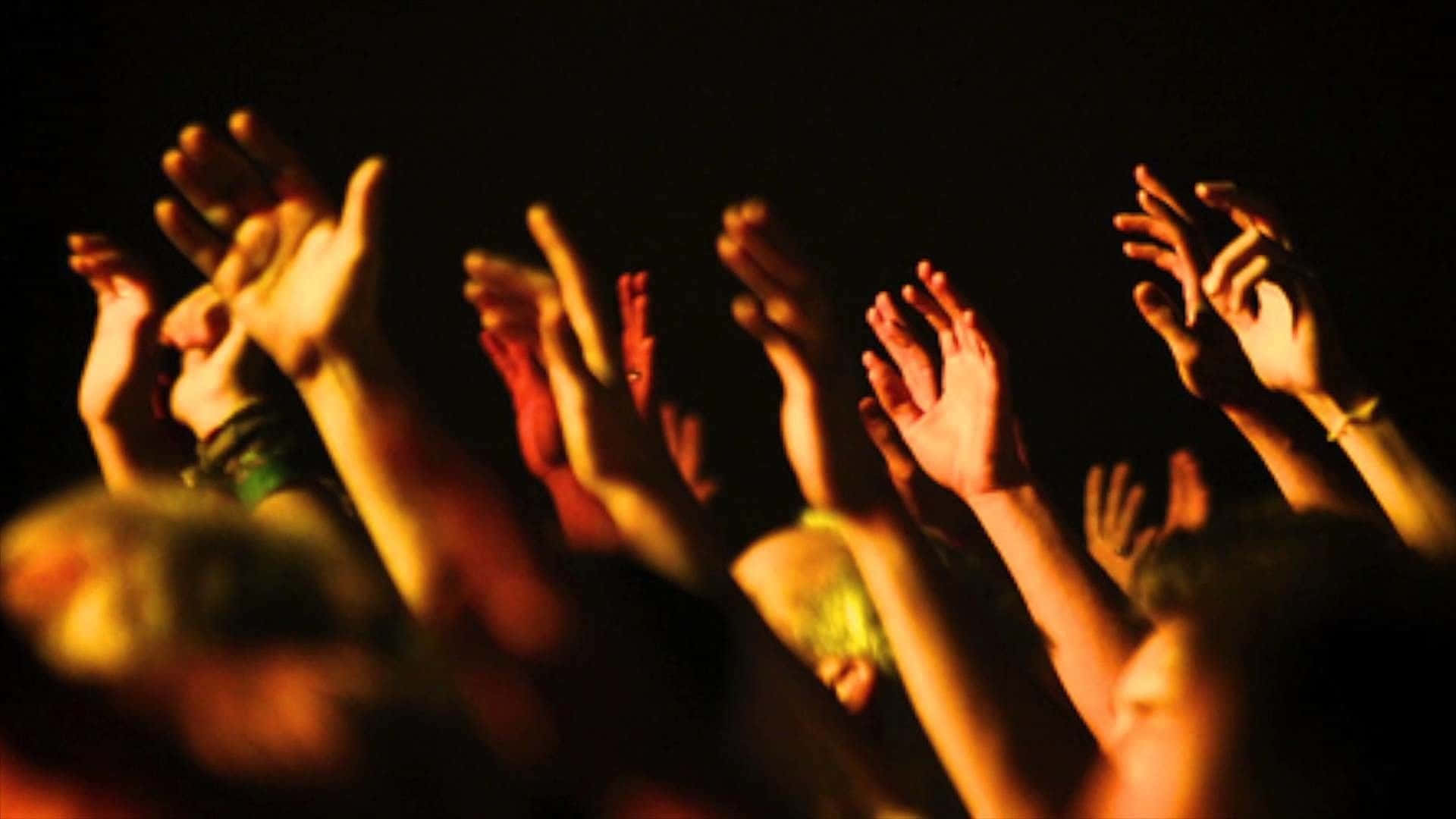 Worship 桌布 壁紙 — 人群高舉雙手，在黑暗背景下被溫暖的舞台燈光照亮。