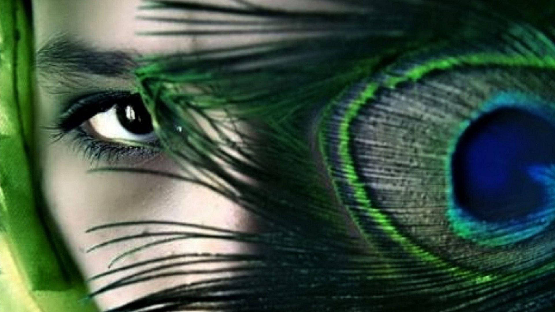 Amazing 桌布 壁紙 — 人類眼睛的特寫，透過充滿活力的綠色和藍色孔雀羽毛窺視，羽毛上有複雜的眼睛圖案。