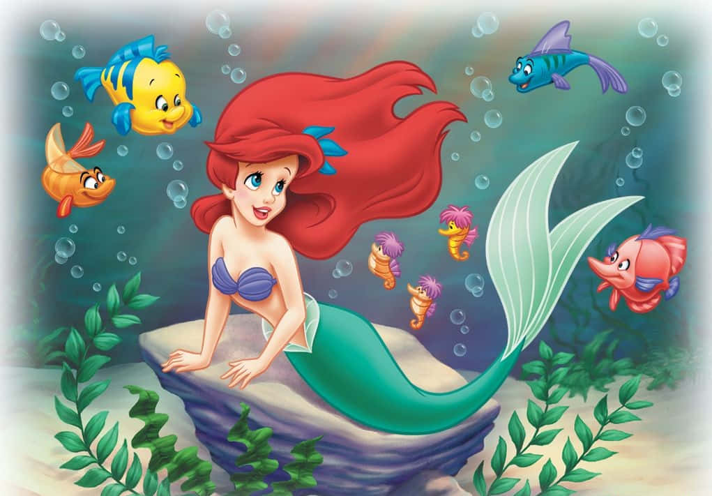 little mermaid 桌布 壁紙 — 人魚公主艾莉兒擁有一頭飄逸的紅髮，坐在岩石上，被色彩繽紛的魚和氣泡環繞的水底場景。