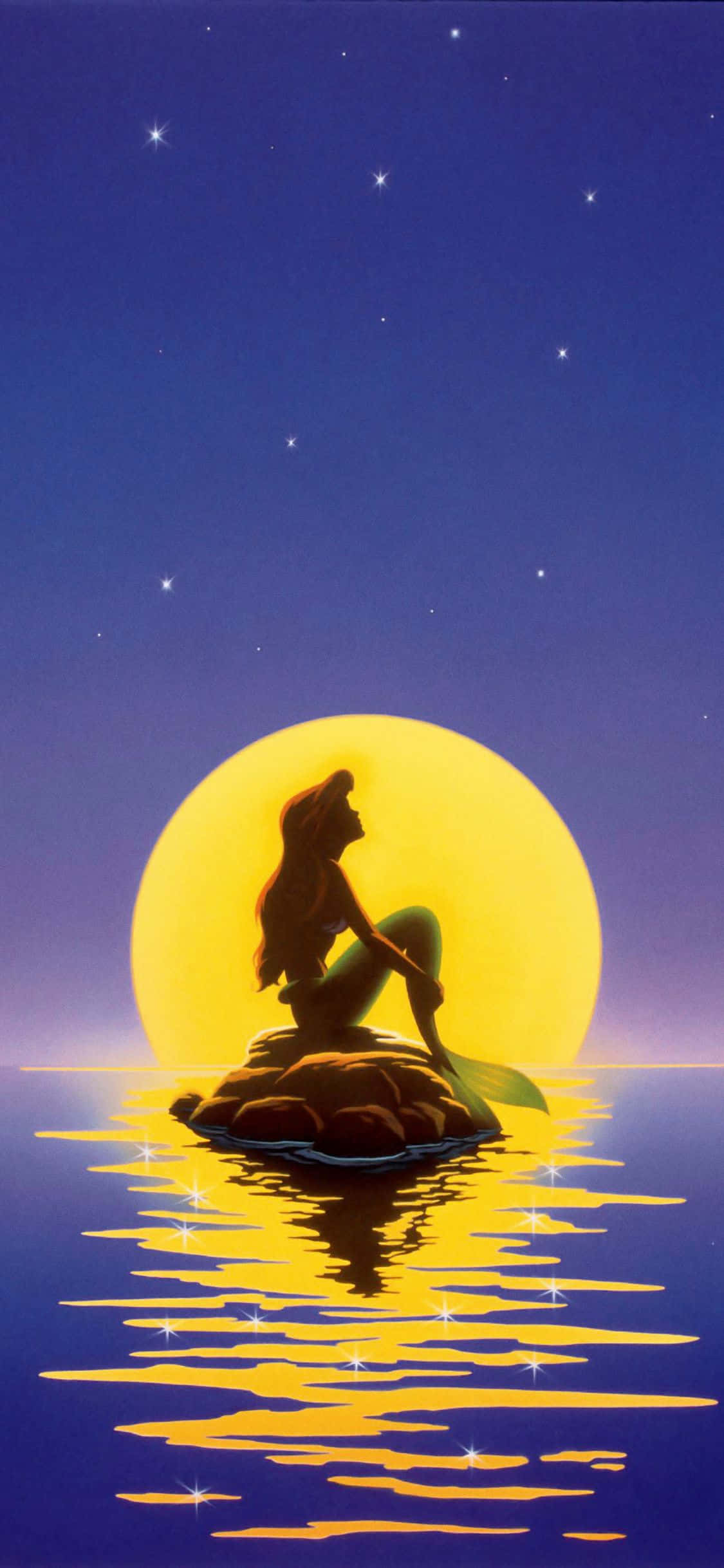 little mermaid 桌布 壁紙 — 人魚剪影坐在岩石上，在閃爍的黃色月亮下，月亮映照在平靜的水面上，背景是繁星點點的夜空。