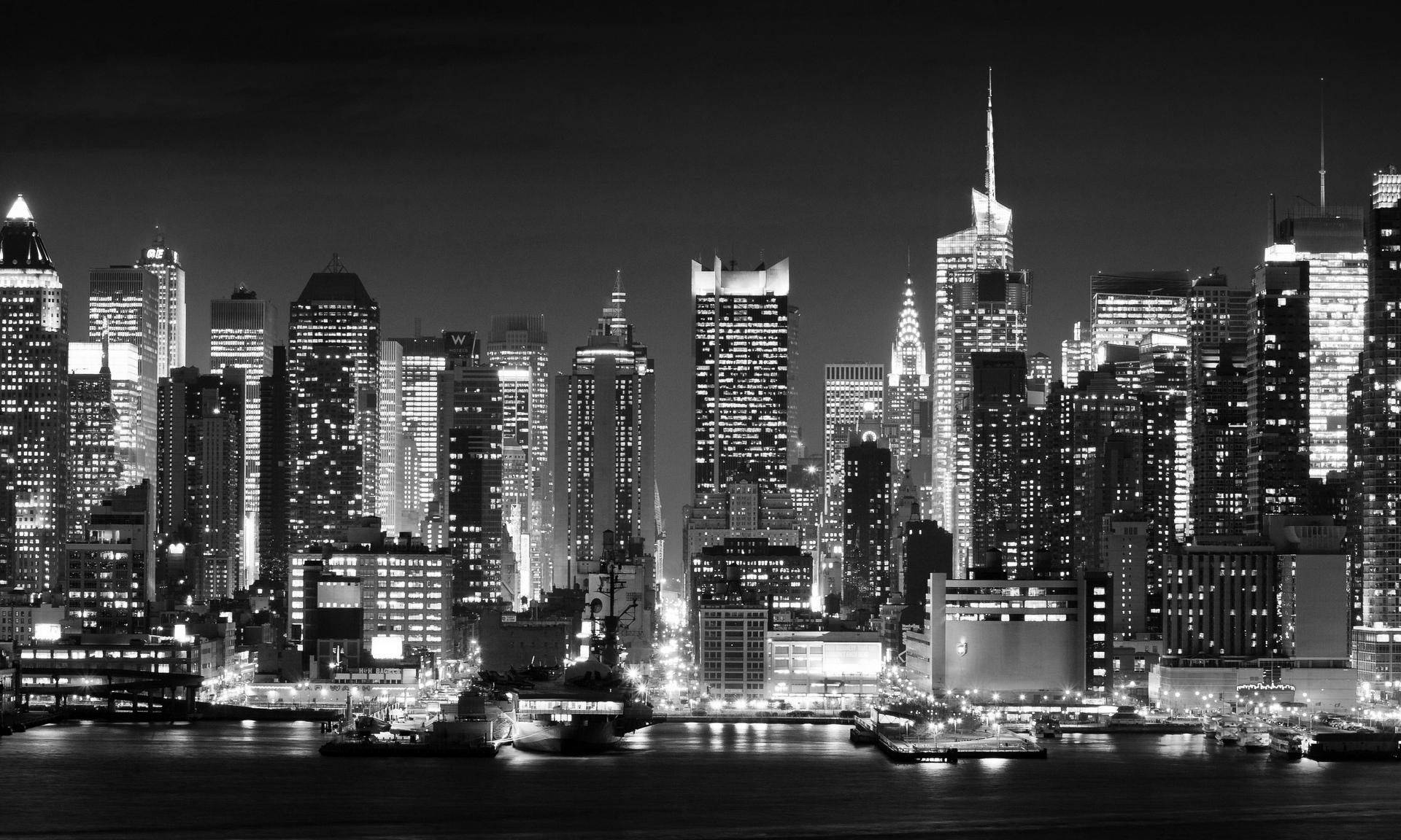New York 桌布 壁紙 — 令人印象深刻的黑白夜景城市景觀，高聳的摩天大樓帶有發光的窗戶，倒映在平靜的水面上。