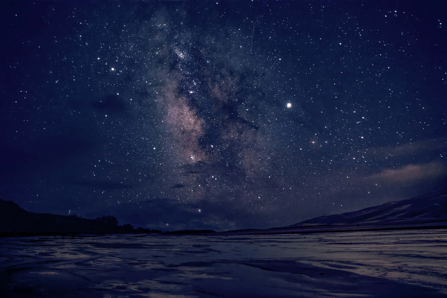 Dark Sky 桌布 壁紙 — 令人嘆為觀止的冬夜天空，充滿無數星星和銀河，拱形在白雪覆蓋的風景和遠處的山脈之上。