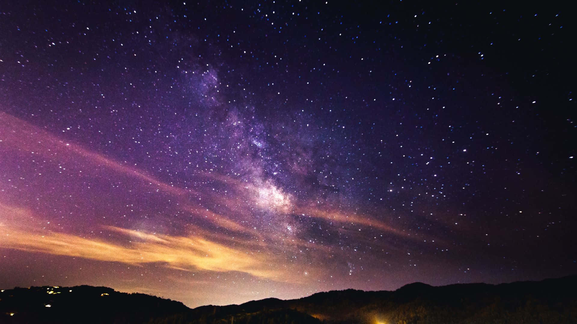 星空動畫 桌布 壁紙 — 令人嘆為觀止的夜空，佈滿星星，銀河在剪影山脈上方拱起，下方有發光的橙色雲彩。