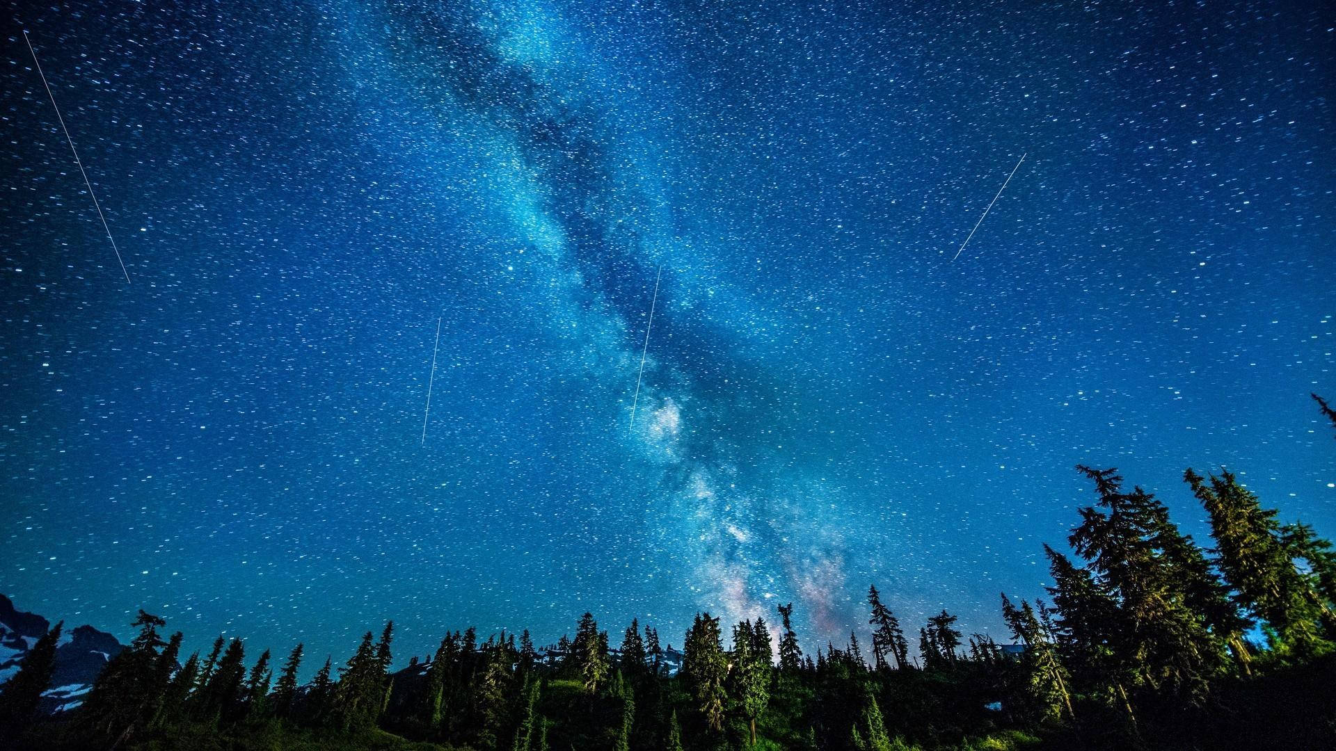 Milky 桌布 壁紙 — 令人嘆為觀止的夜空，佈滿星星，銀河在黑暗的森林剪影和遠處的雪山上方拱起。