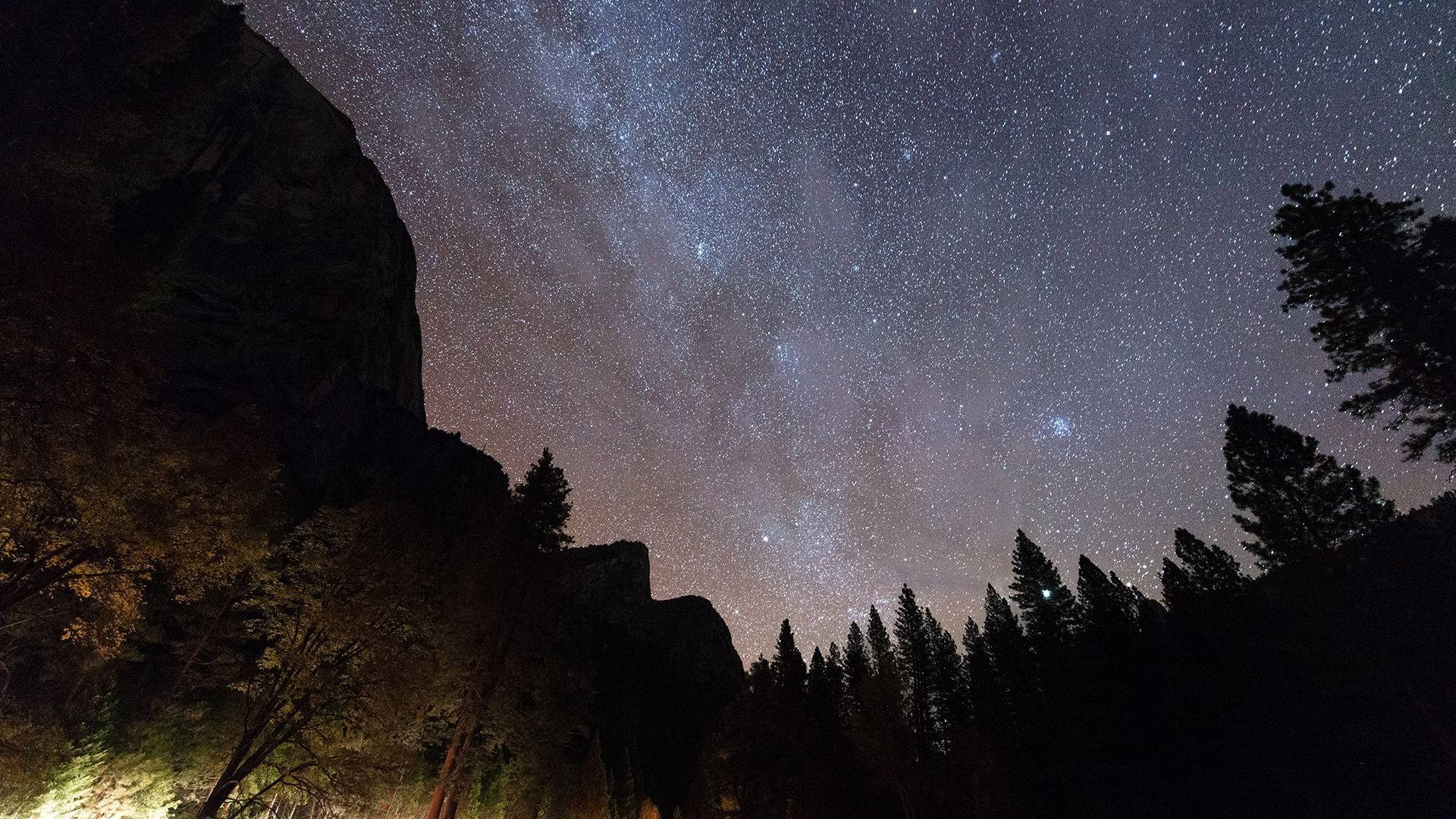 Redwood 桌布 壁紙 — 令人嘆為觀止的夜空，佈滿無數星星，銀河在黑暗的樹木和岩石懸崖上拱起。