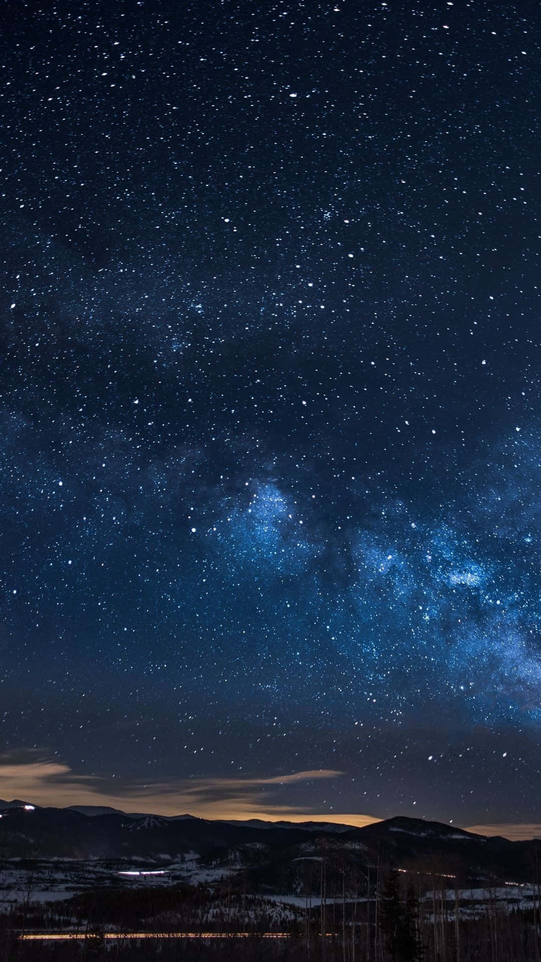 Starry Sky 桌布 壁紙 — 令人嘆為觀止的夜空，佈滿無數星星，閃爍的銀河在積雪的山脈和遠處的小鎮上空拱起。