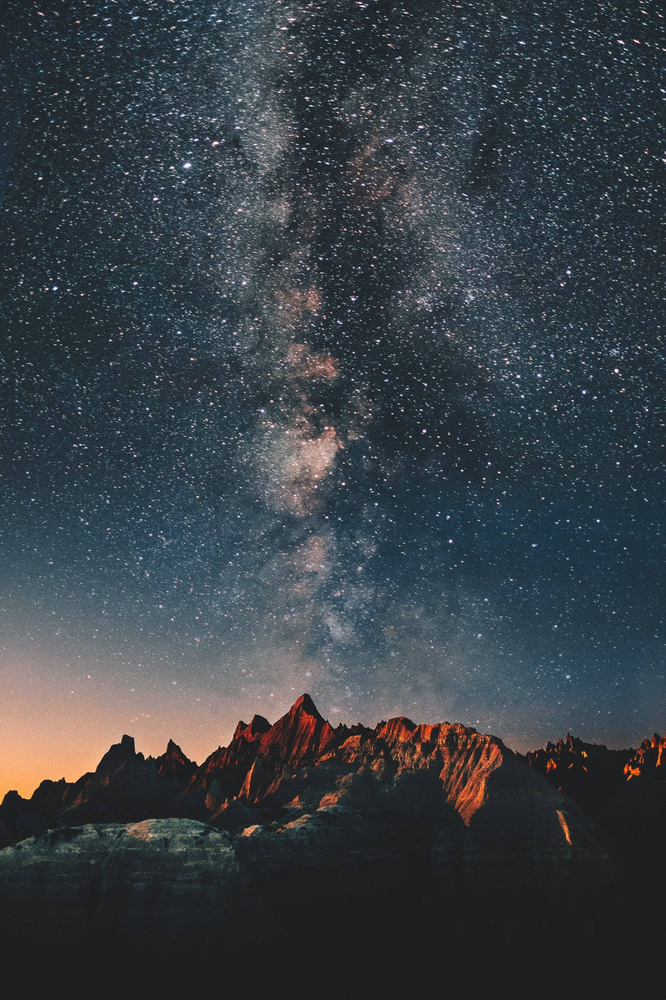夜空 桌布 壁紙 — 令人嘆為觀止的夜空，佈滿無數繁星，銀河在溫暖橙色光芒照耀的崎嶇山峰上拱起。