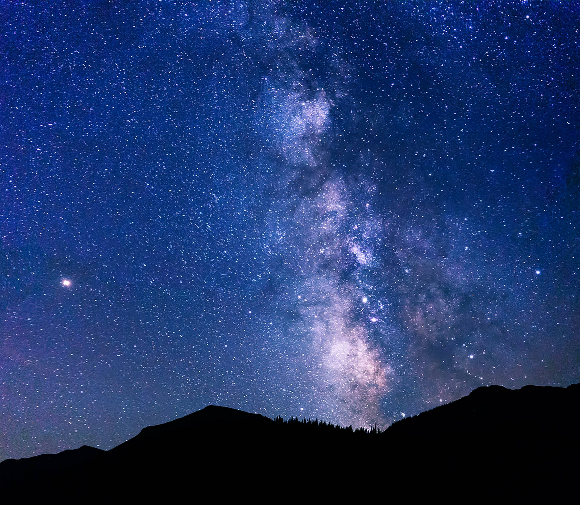 夜空 桌布 壁紙 — 令人嘆為觀止的夜空，充滿無數星星，發光的銀河在黑暗的山脈輪廓上拱起。