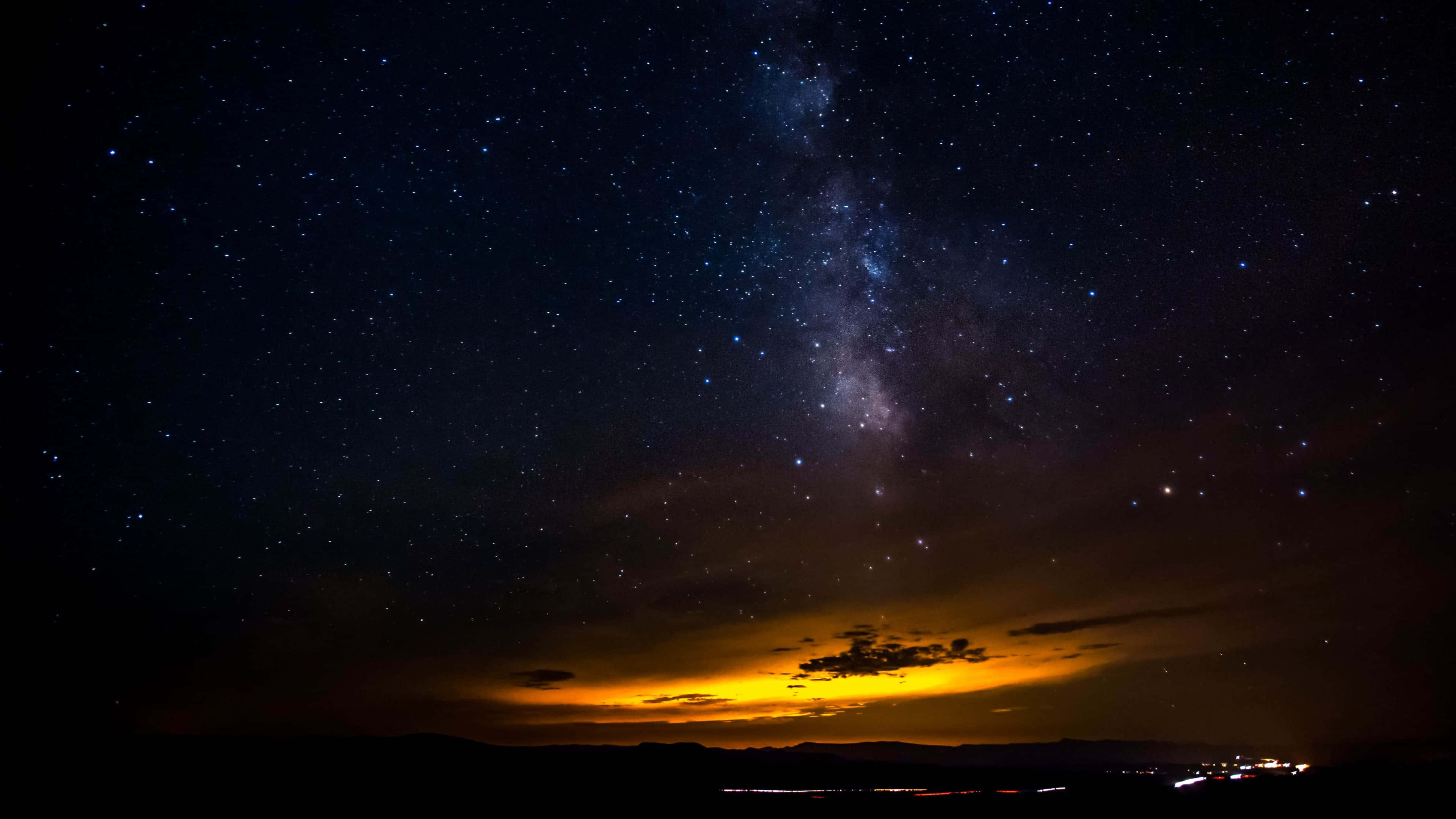 夜空 桌布 壁紙 — 令人嘆為觀止的夜空，充滿無數星星和銀河，拱形跨越剪影山脈，地平線上有溫暖的橙色光芒。