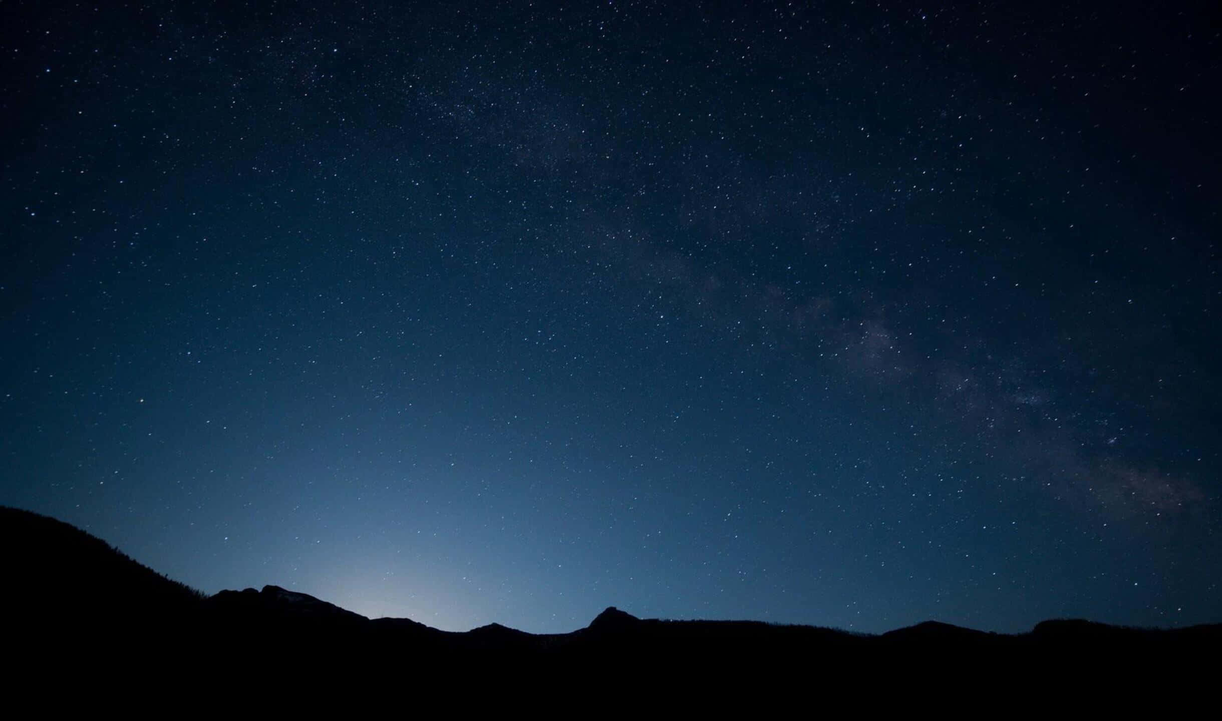夜空 桌布 壁紙 — 令人嘆為觀止的夜空，充滿無數星星和銀河，拱形跨越黑暗的山脈輪廓。