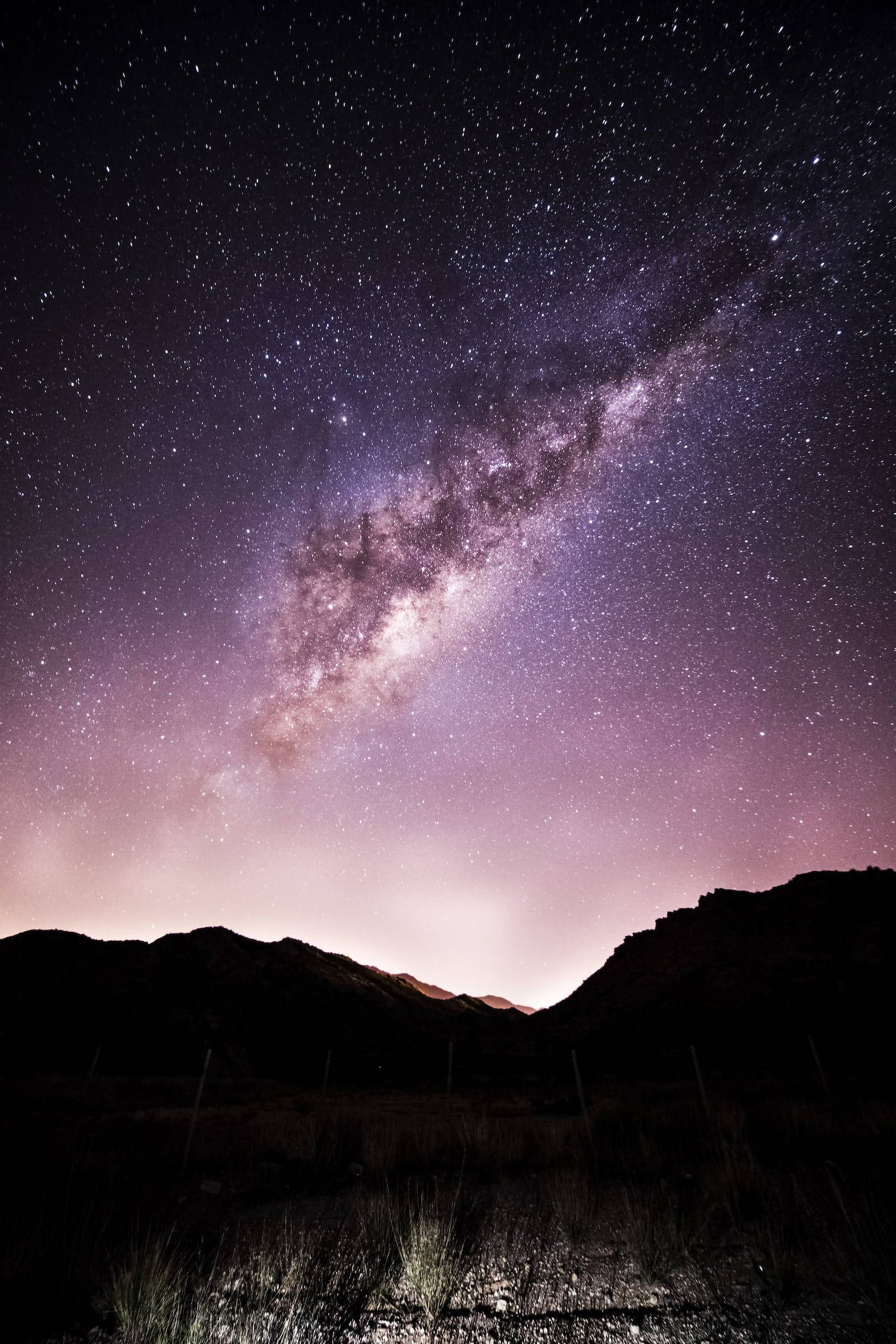 Purple Galaxy 桌布 壁紙 — 令人嘆為觀止的夜空，滿天繁星，銀河在黑暗的山巒剪影上拱起。