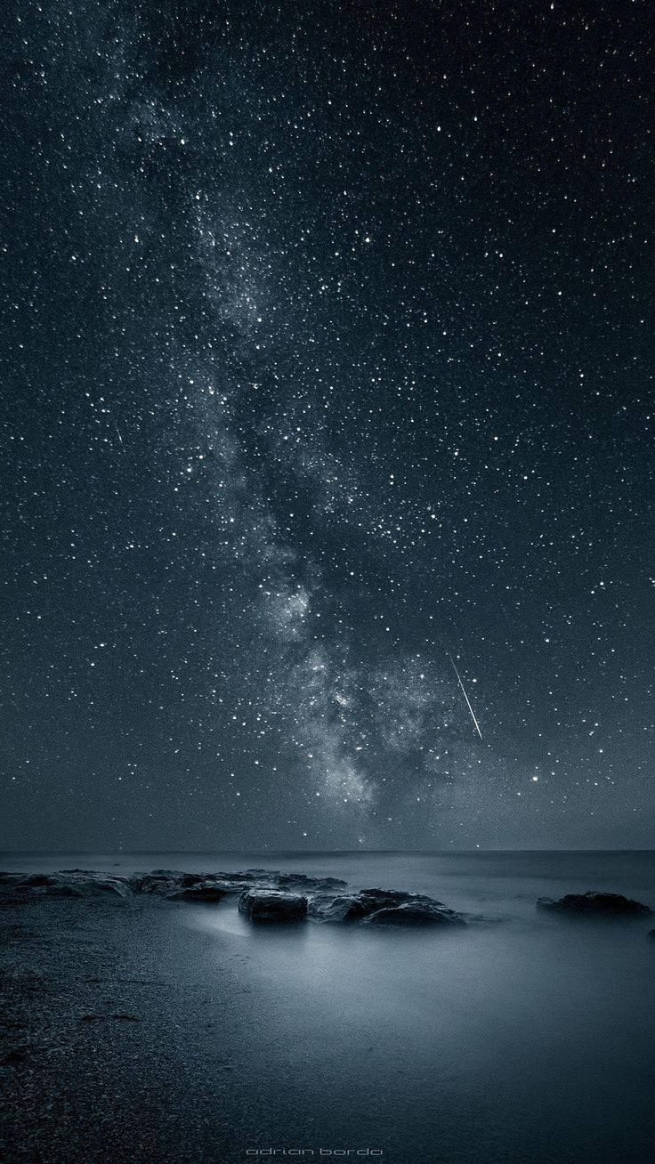 手機 桌布 壁紙 — 令人嘆為觀止的夜空，繁星點點，銀河在平靜的海洋和前景的黑色岩石上拱起。