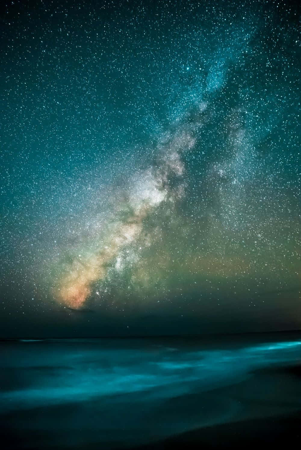 Galaxy Blue Aesthetic 桌布 壁紙 — 令人嘆為觀止的夜空佈滿星星，銀河在閃爍的藍綠色海洋上空拱起。