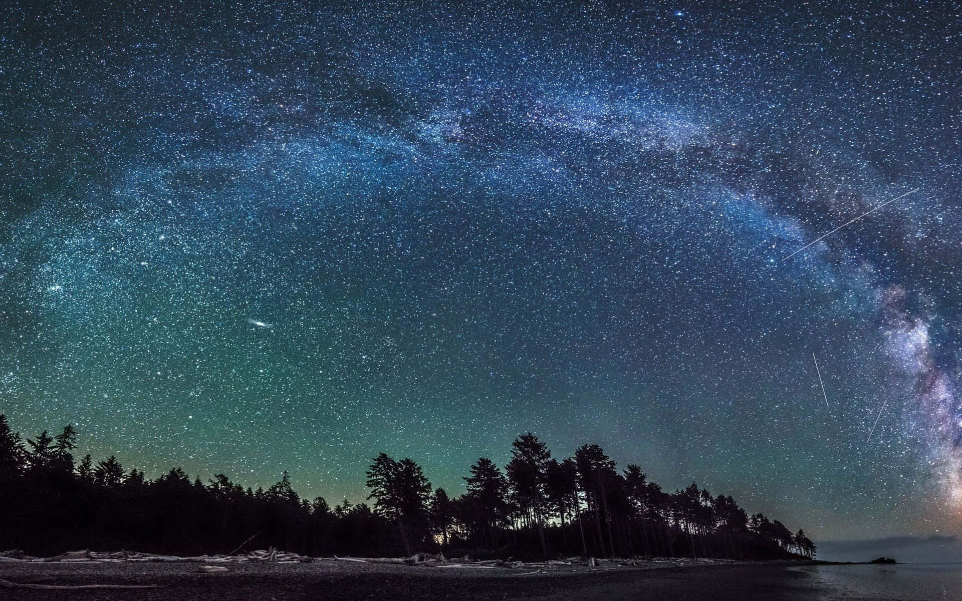 銀河 桌布 壁紙 — 令人嘆為觀止的夜空佈滿星星，銀河在水邊的黑暗森林輪廓上拱起。