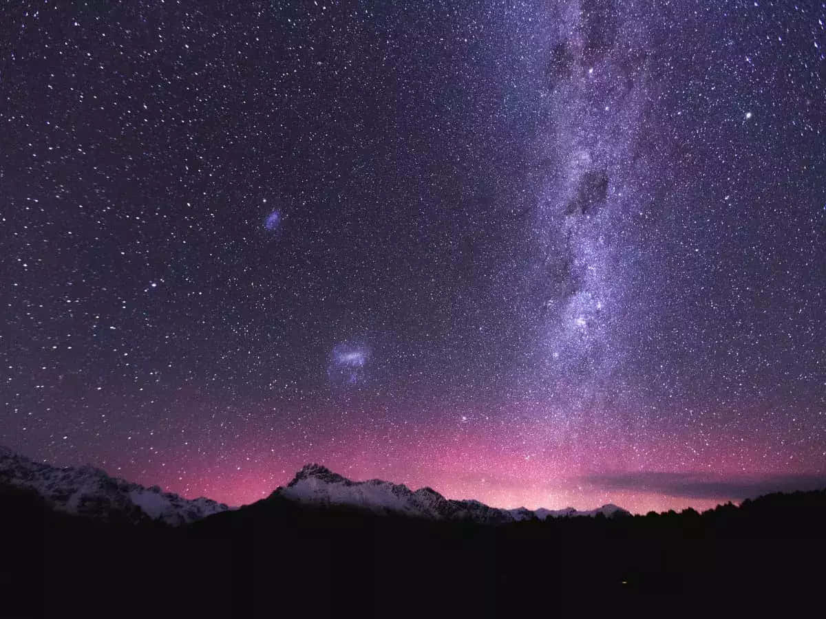 Dark Sky 桌布 壁紙 — 令人嘆為觀止的夜空佈滿繁星，銀河在充滿活力的粉紅色極光下拱起在積雪的山峰之上。