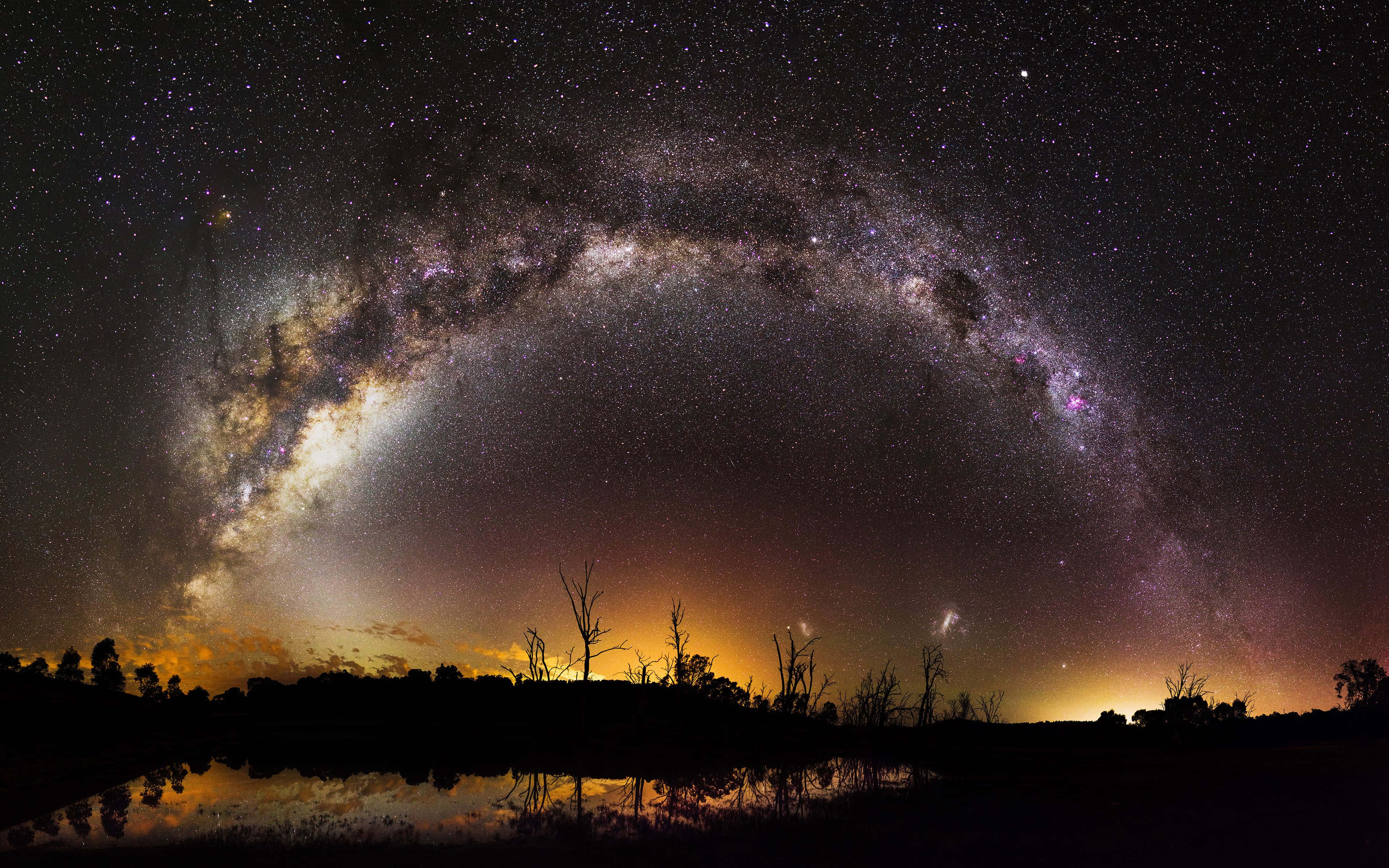 Starry Night Sky 桌布 壁紙 — 令人嘆為觀止的夜空在平靜的水面上拱起，倒映著銀河和發光的橙色地平線。