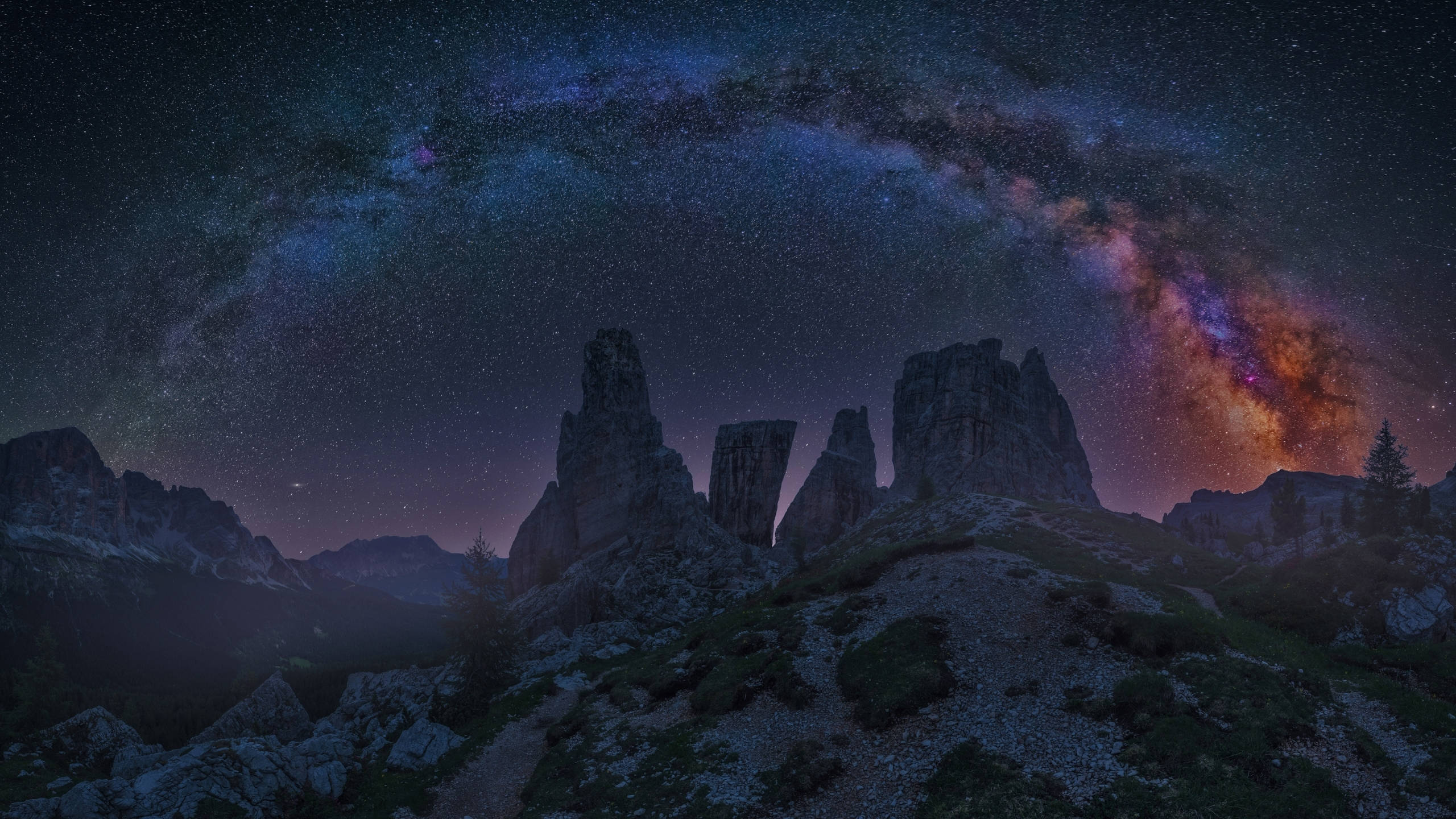 2560x1440 nature 桌布 壁紙 — 令人嘆為觀止的夜空拱起在鋸齒狀的山峰之上，銀河閃耀著鮮豔的紫色和藍色。