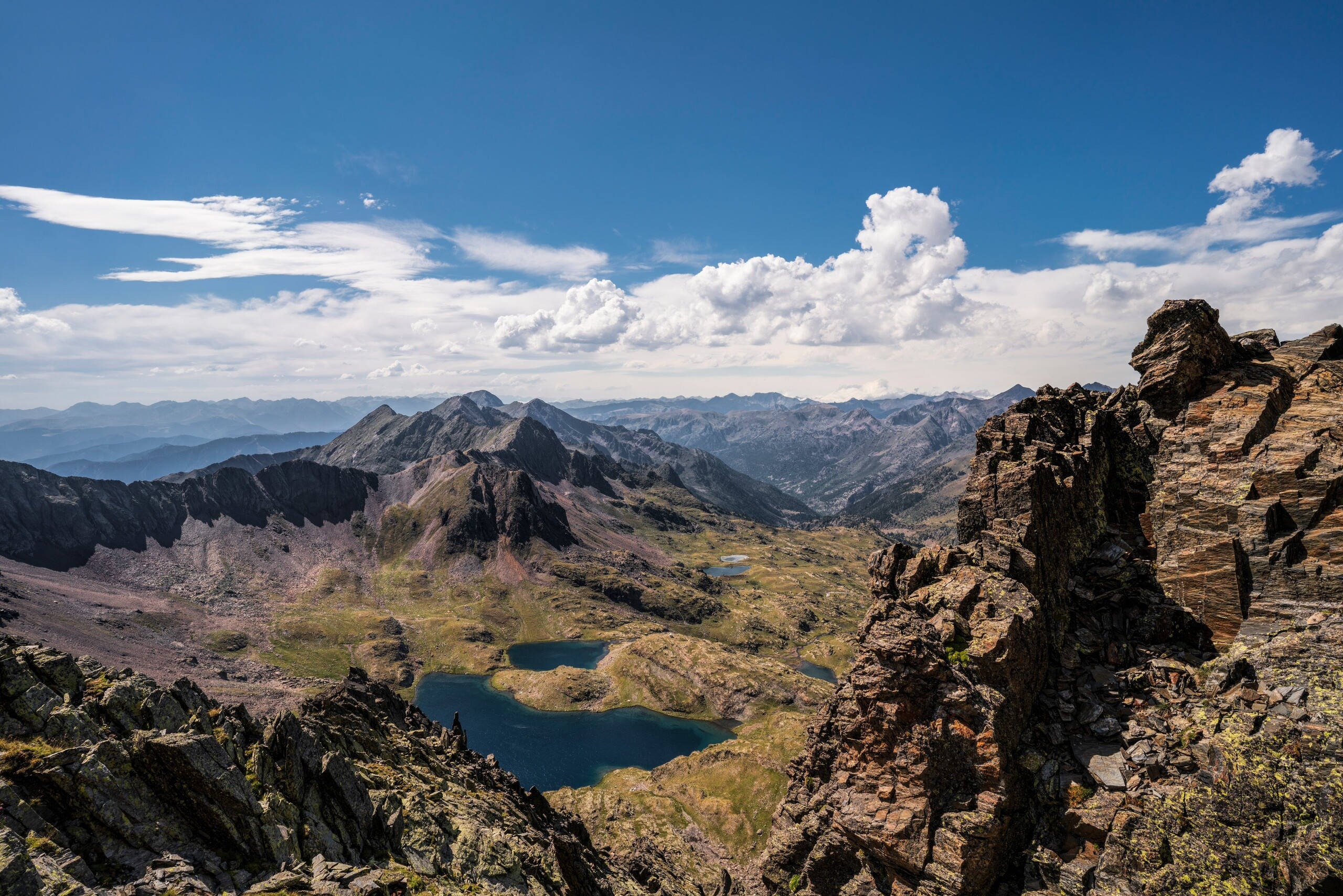 Lake 桌布 壁紙 — 令人嘆為觀止的山景，有鋸齒狀的山峰、崎嶇的懸崖和深藍色的高山湖泊，在明亮的藍天下有蓬鬆的白雲。